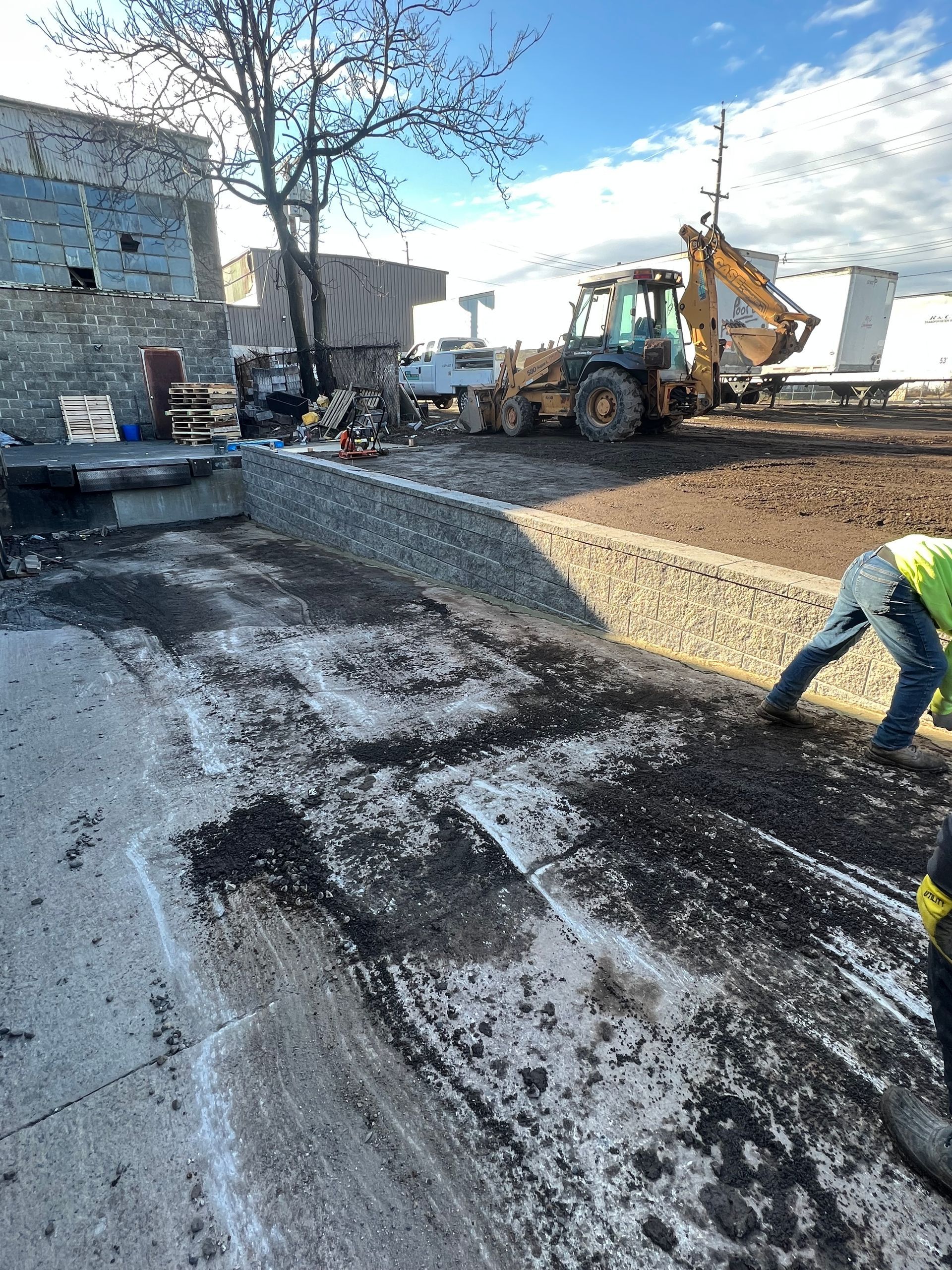 A man is working on a construction site with a tractor in the background.