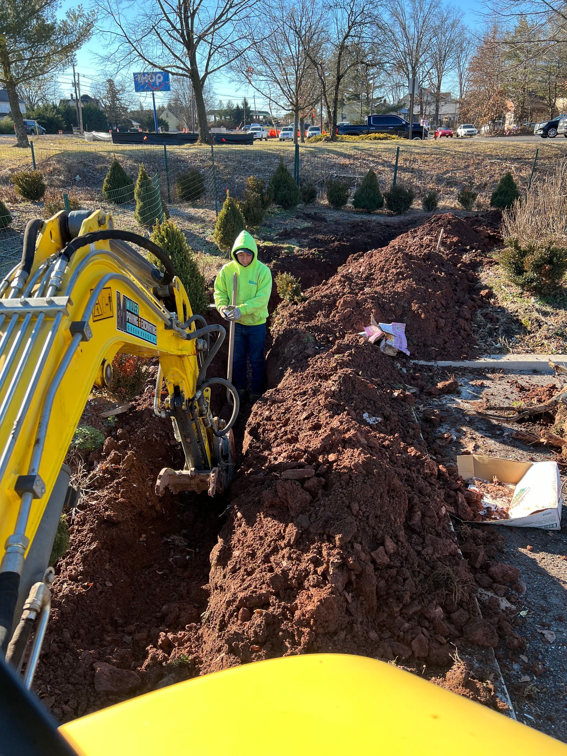 A man is digging in the dirt next to a yellow excavator.