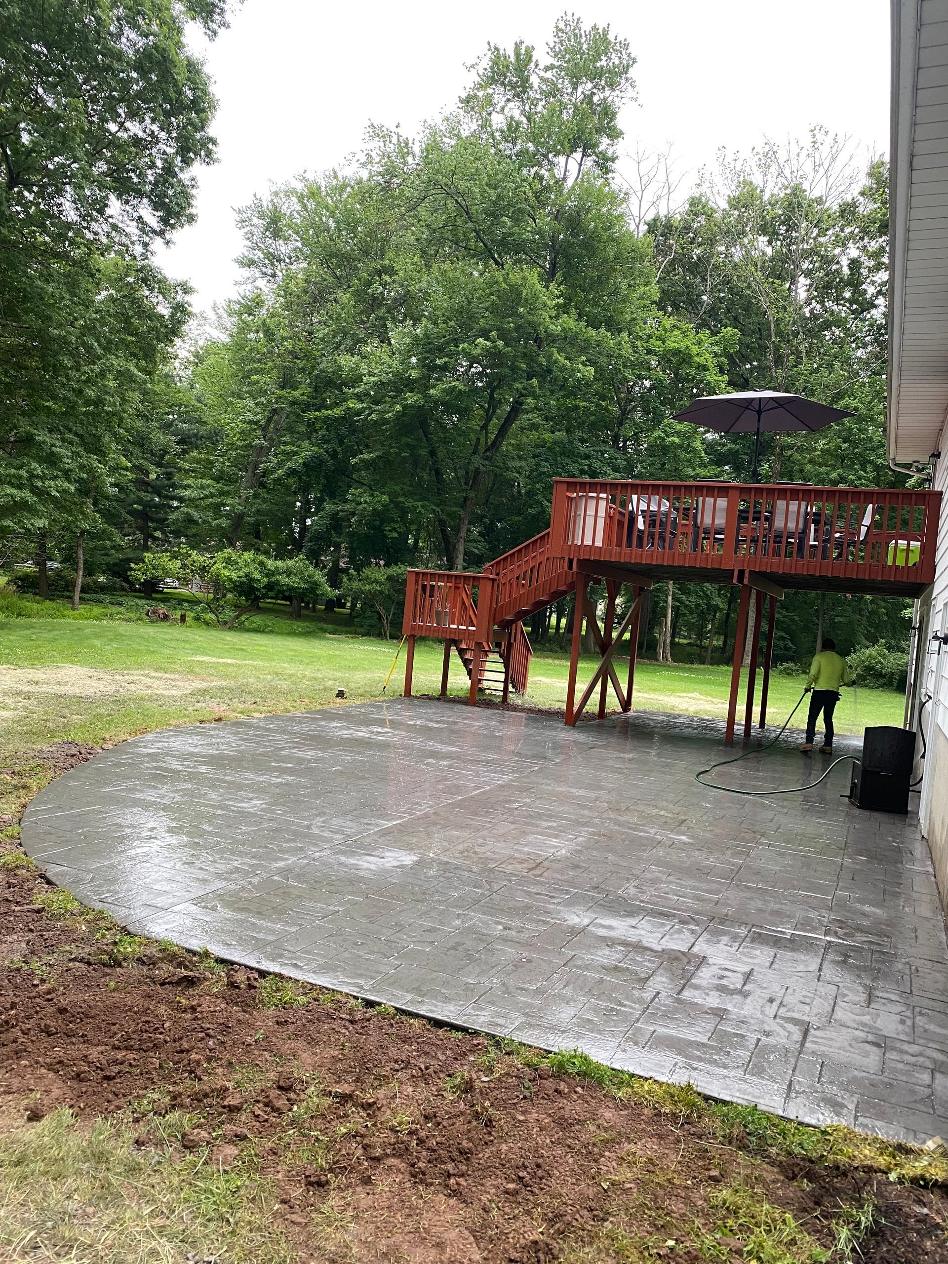 A patio with a wooden deck and stairs in the backyard of a house.