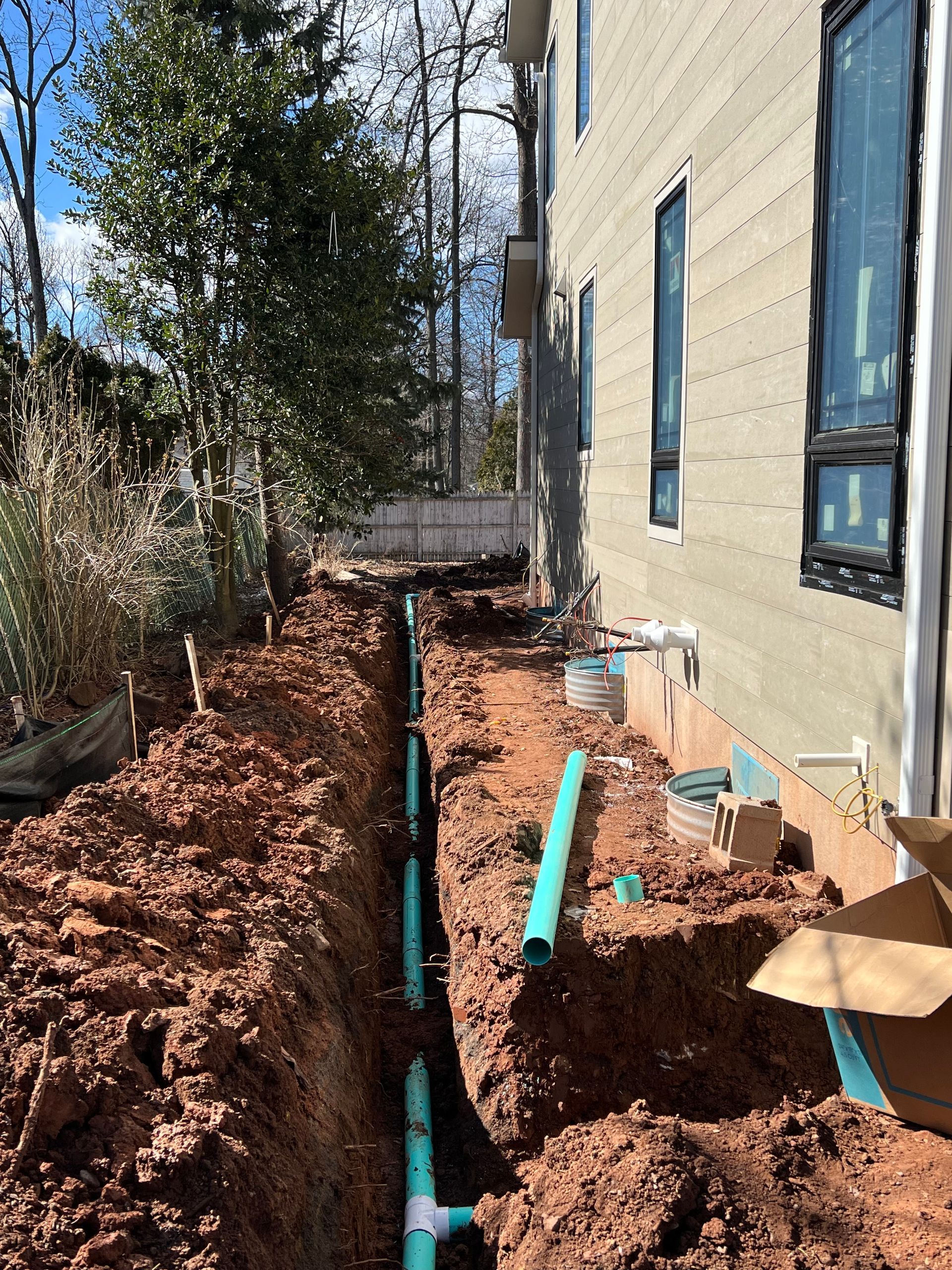 A green pipe is being installed in the dirt in front of a house.