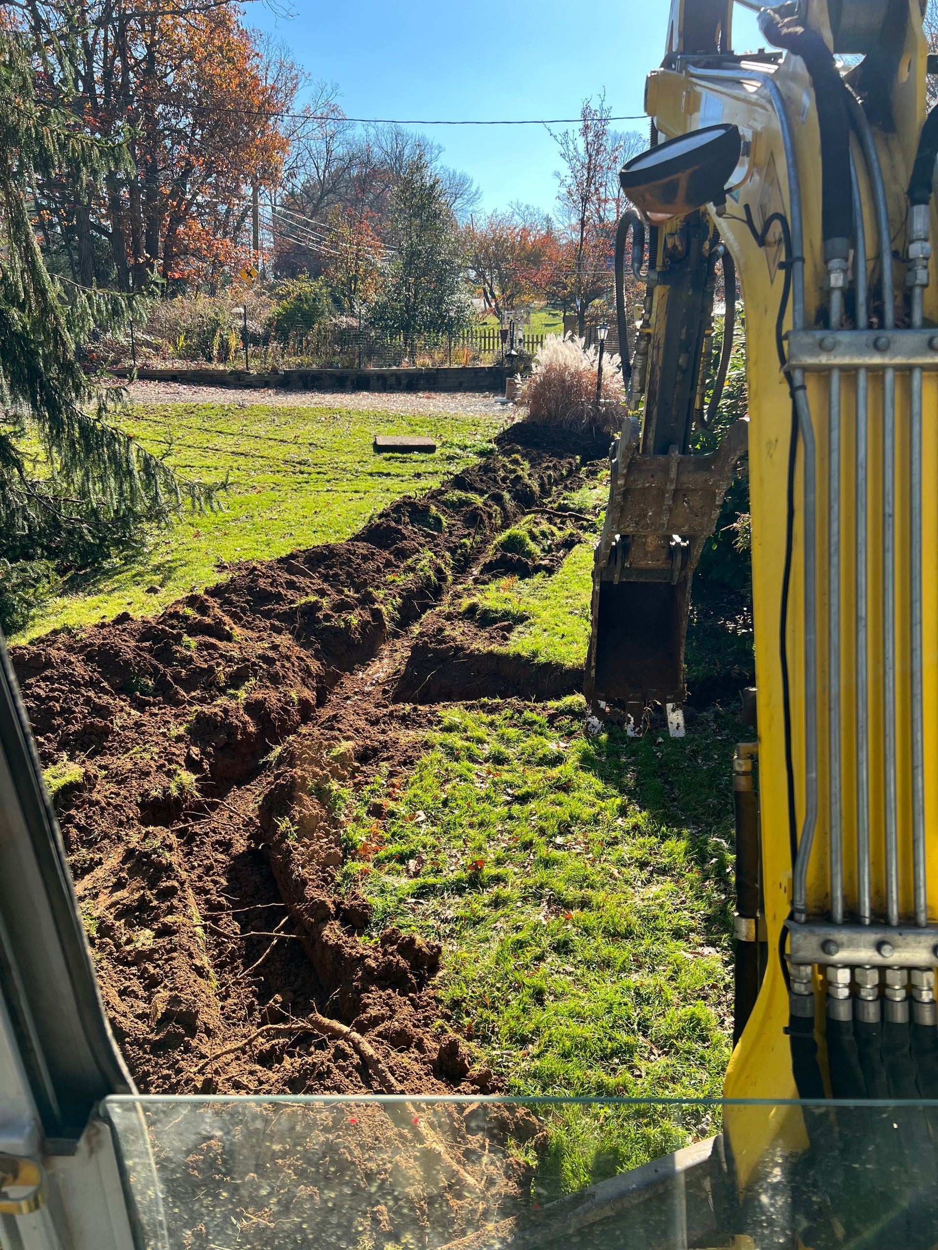 A yellow excavator is digging a hole in a grassy field.