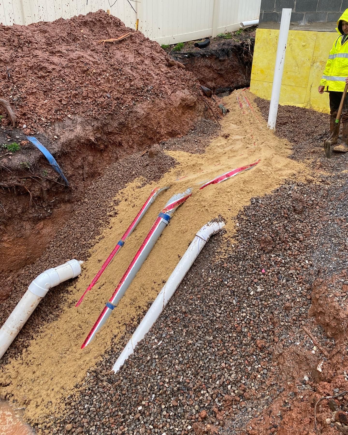 A man is standing next to a pile of dirt and pipes.