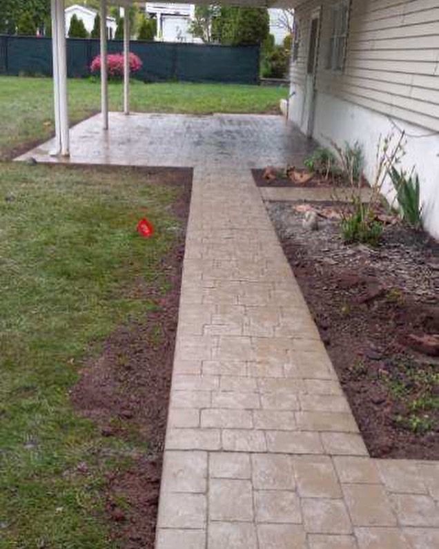 A brick walkway leading to a covered patio in the backyard of a house.