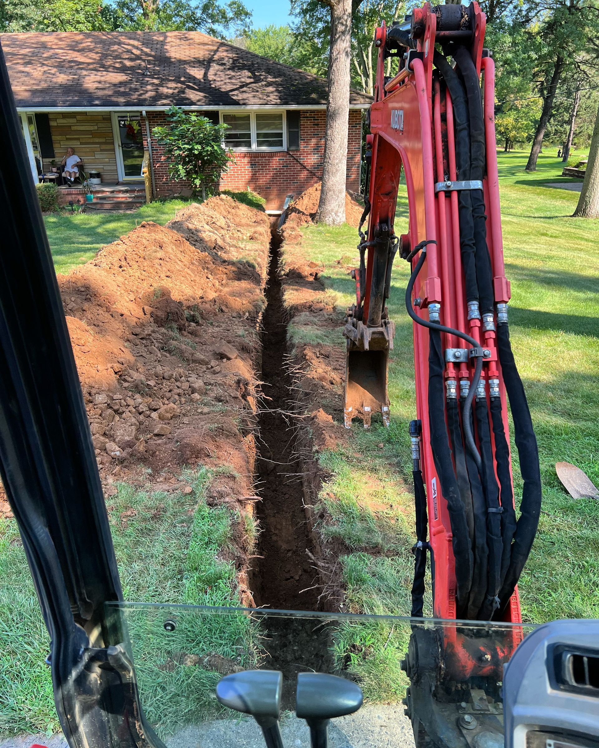 A red excavator is digging a hole in the ground in front of a house.
