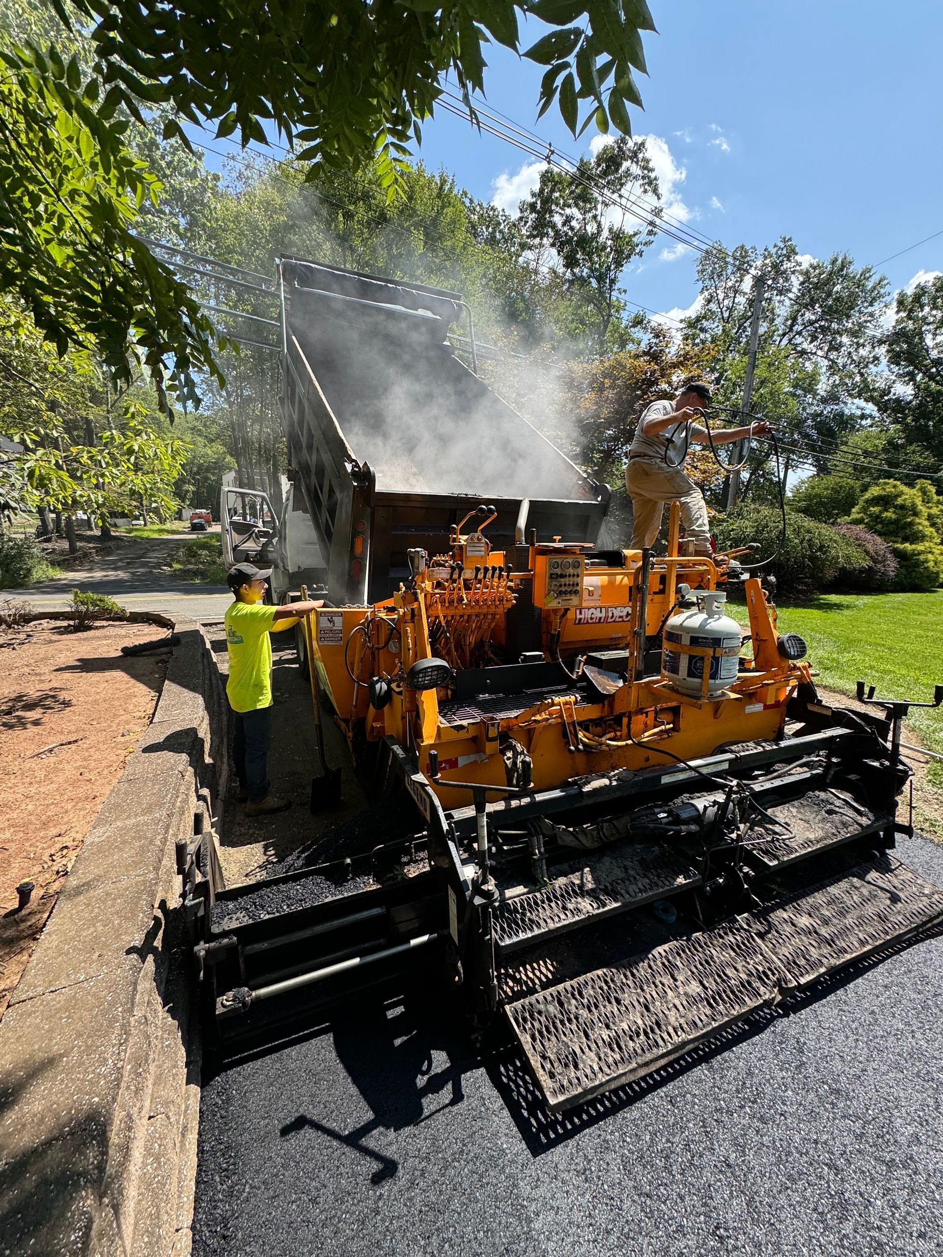A man is standing next to a machine that is spreading asphalt on a road.