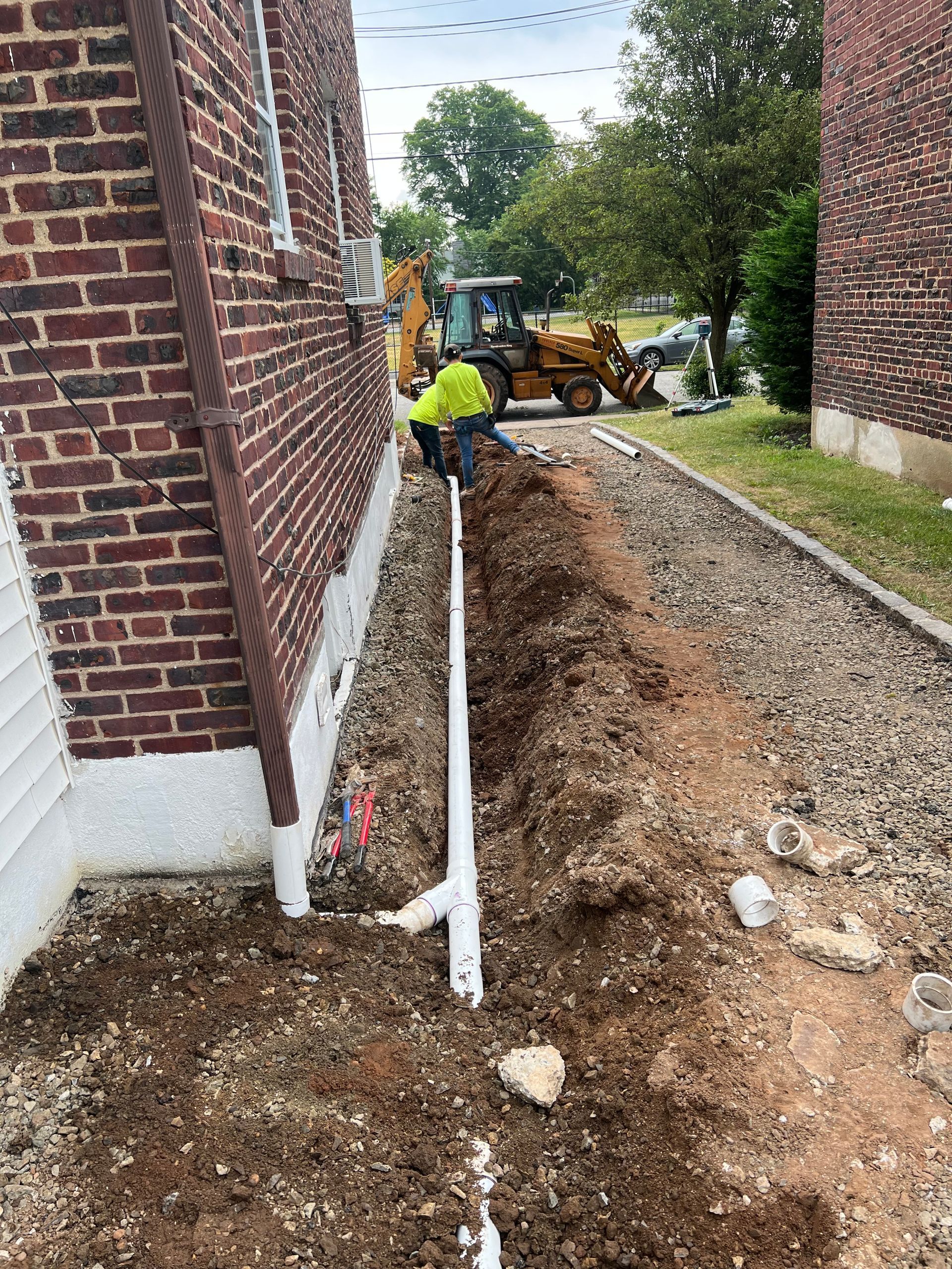 A man is digging a hole in the ground next to a brick building.