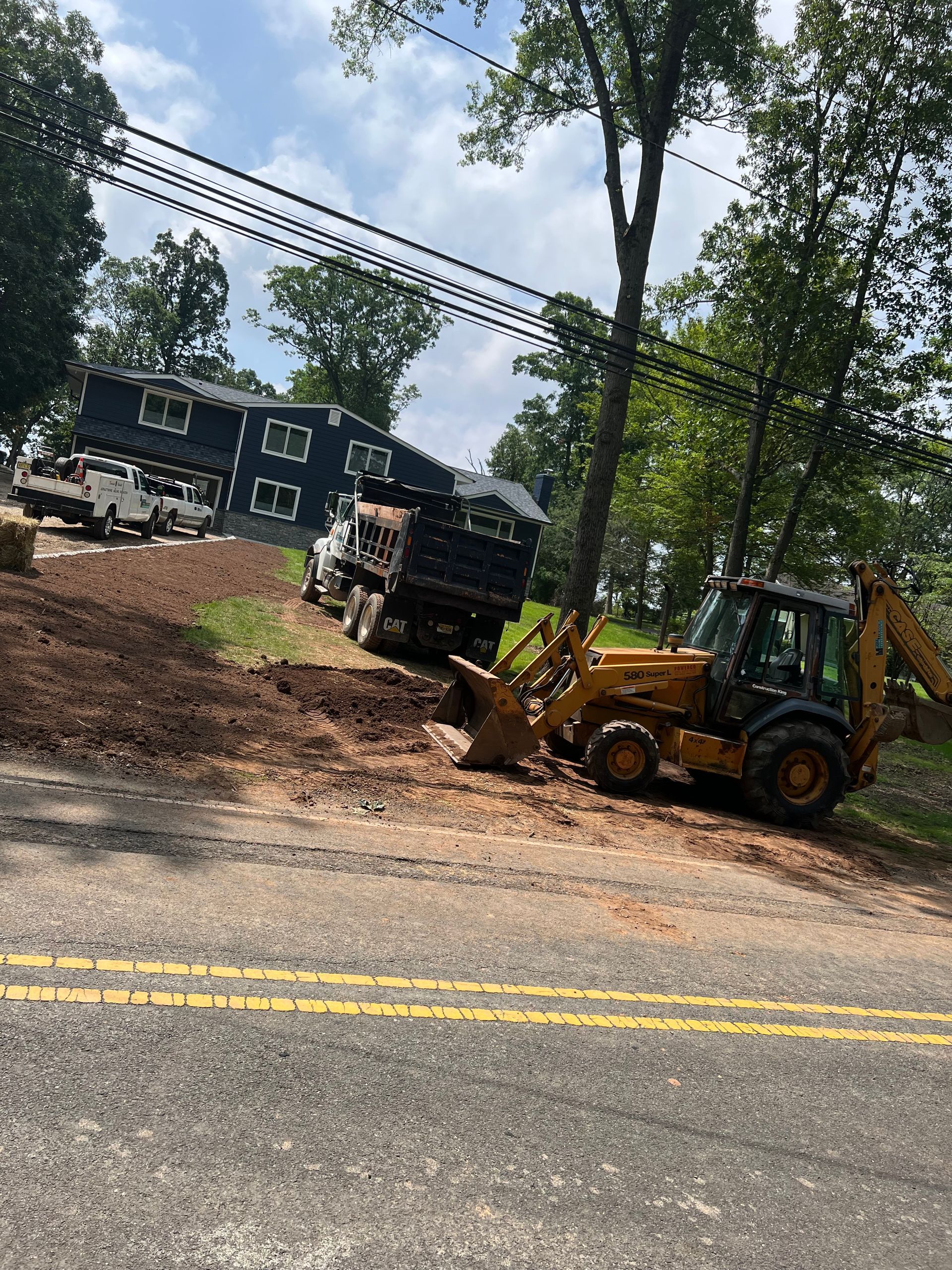 A bulldozer is sitting on the side of the road next to a dump truck.