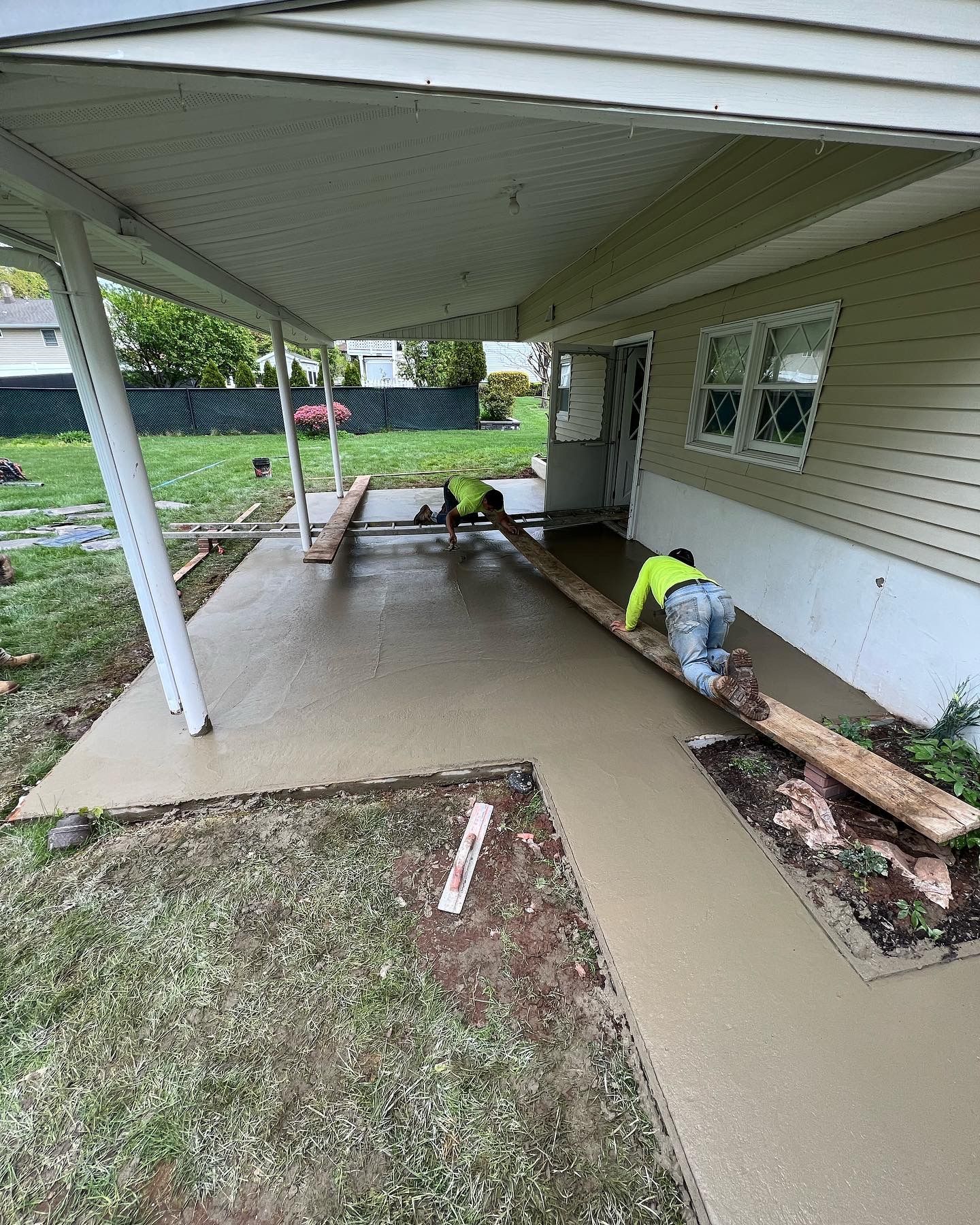 A couple of men are working on a concrete walkway in front of a house.