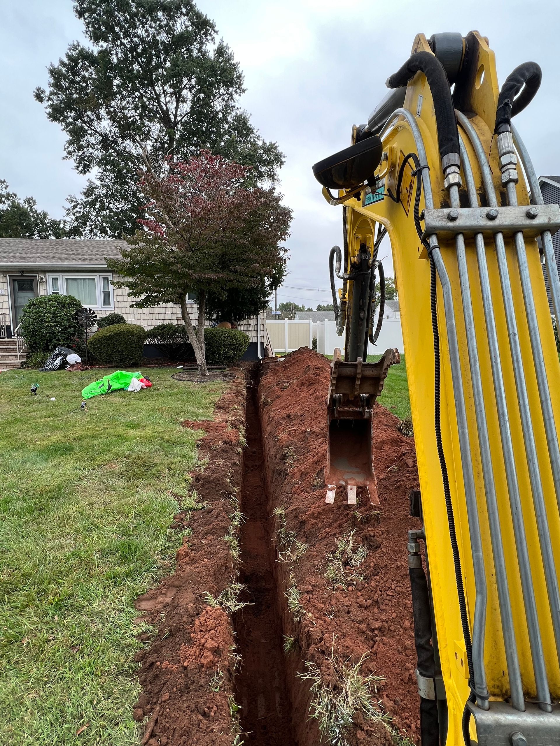 A yellow excavator is digging a trench in a yard.