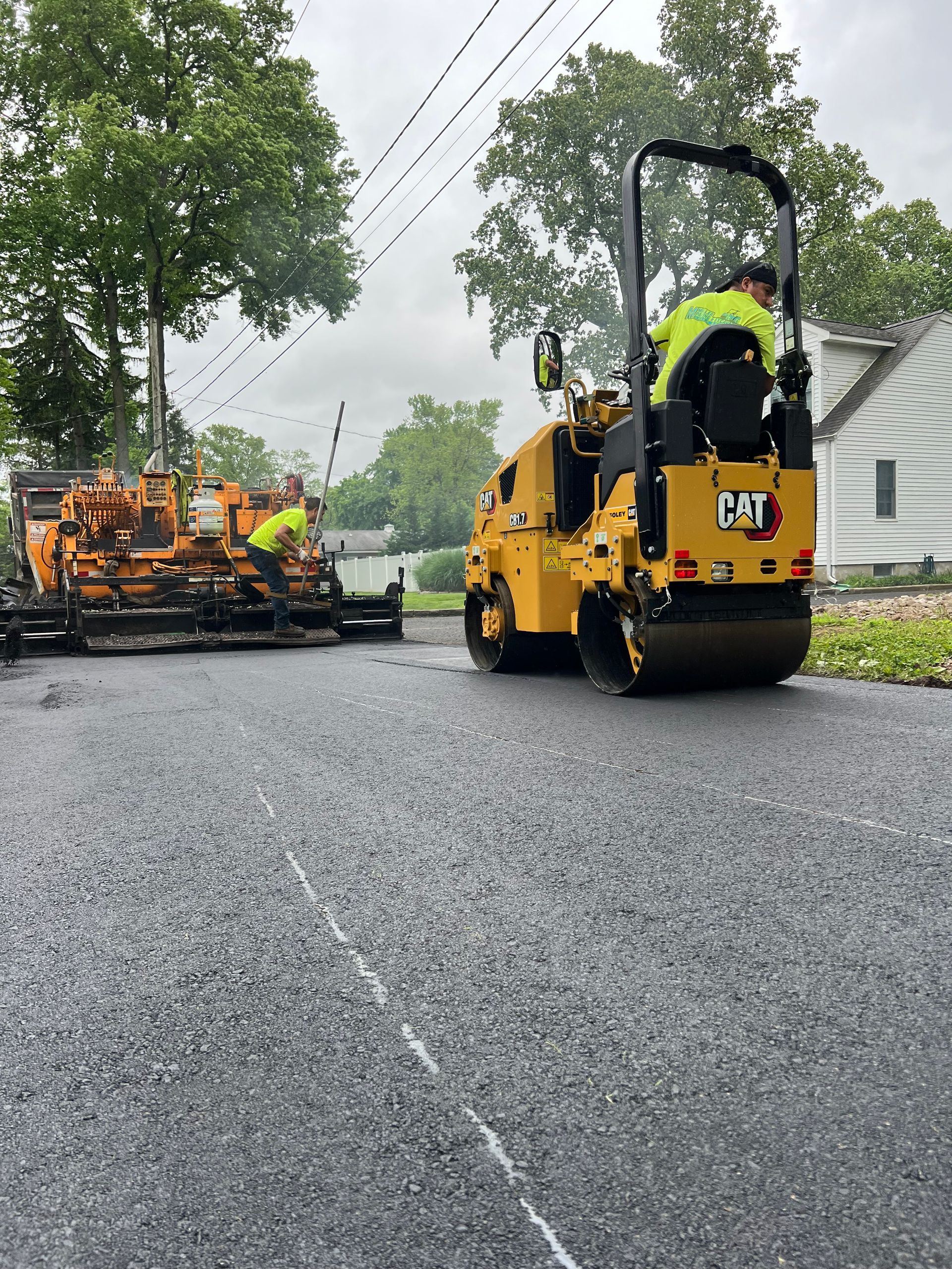 A man is driving a yellow cat roller on a road.