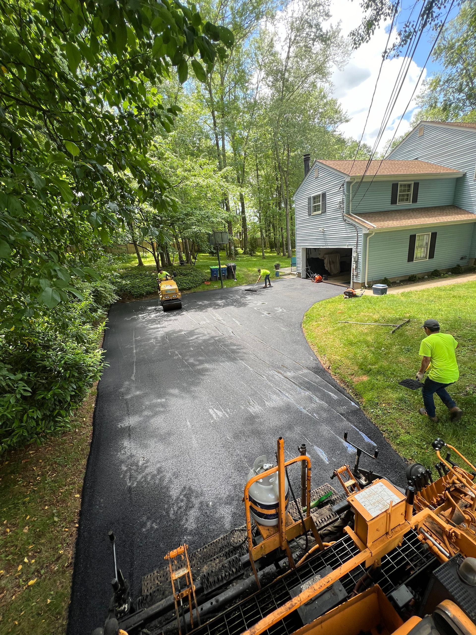 A man is standing next to a machine that is paving a driveway in front of a house.