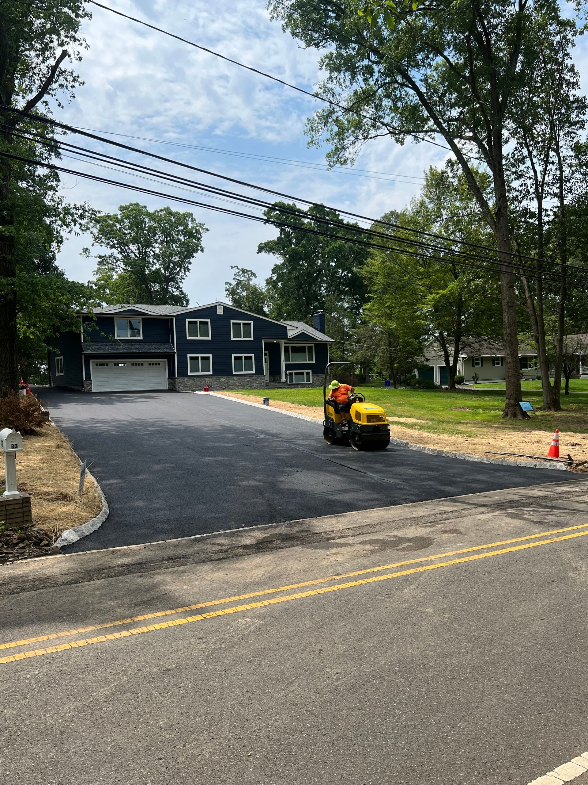 A man is driving a tractor down a road in front of a house.