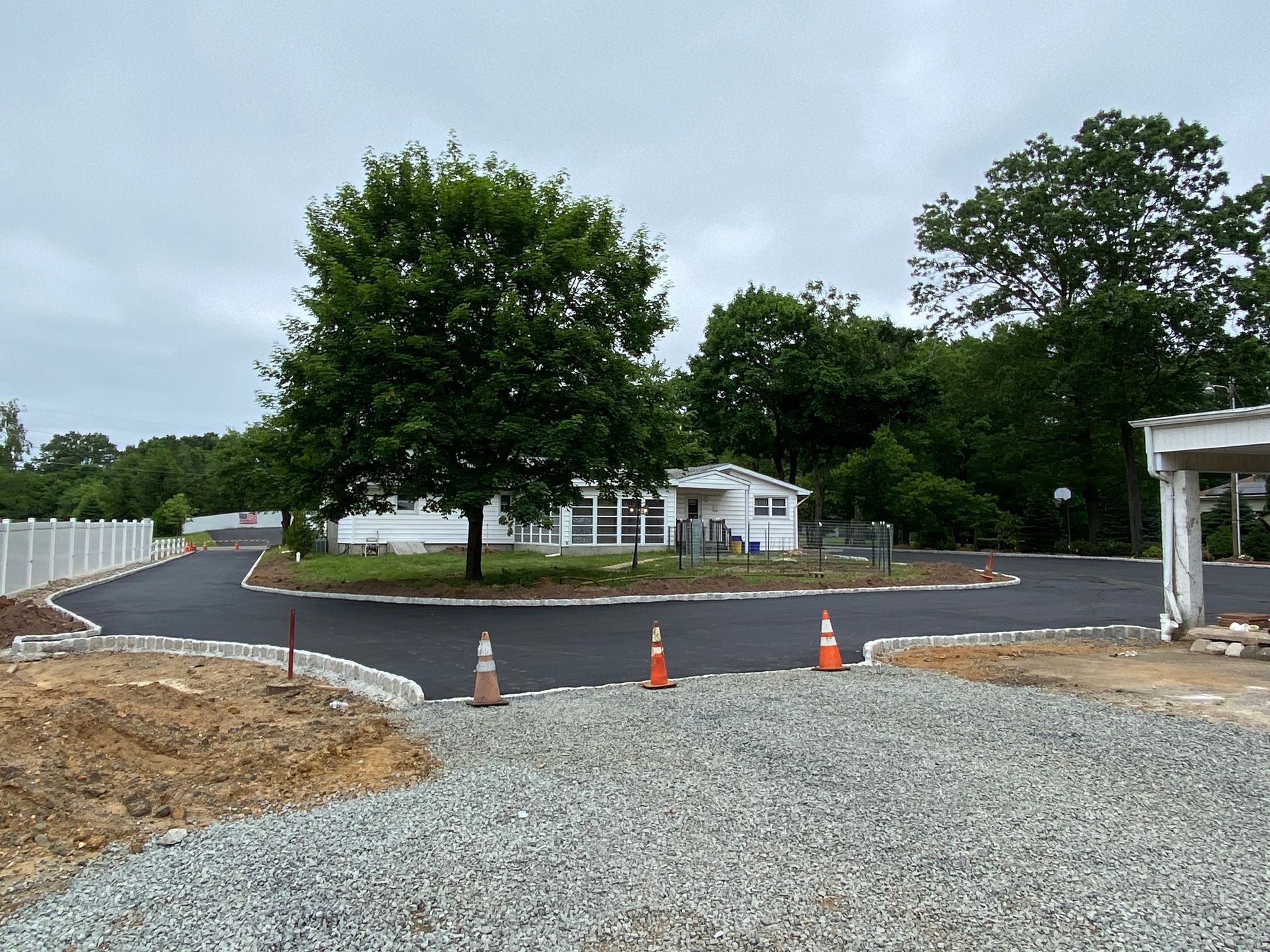 A gravel driveway leading to a house with a tree in the middle