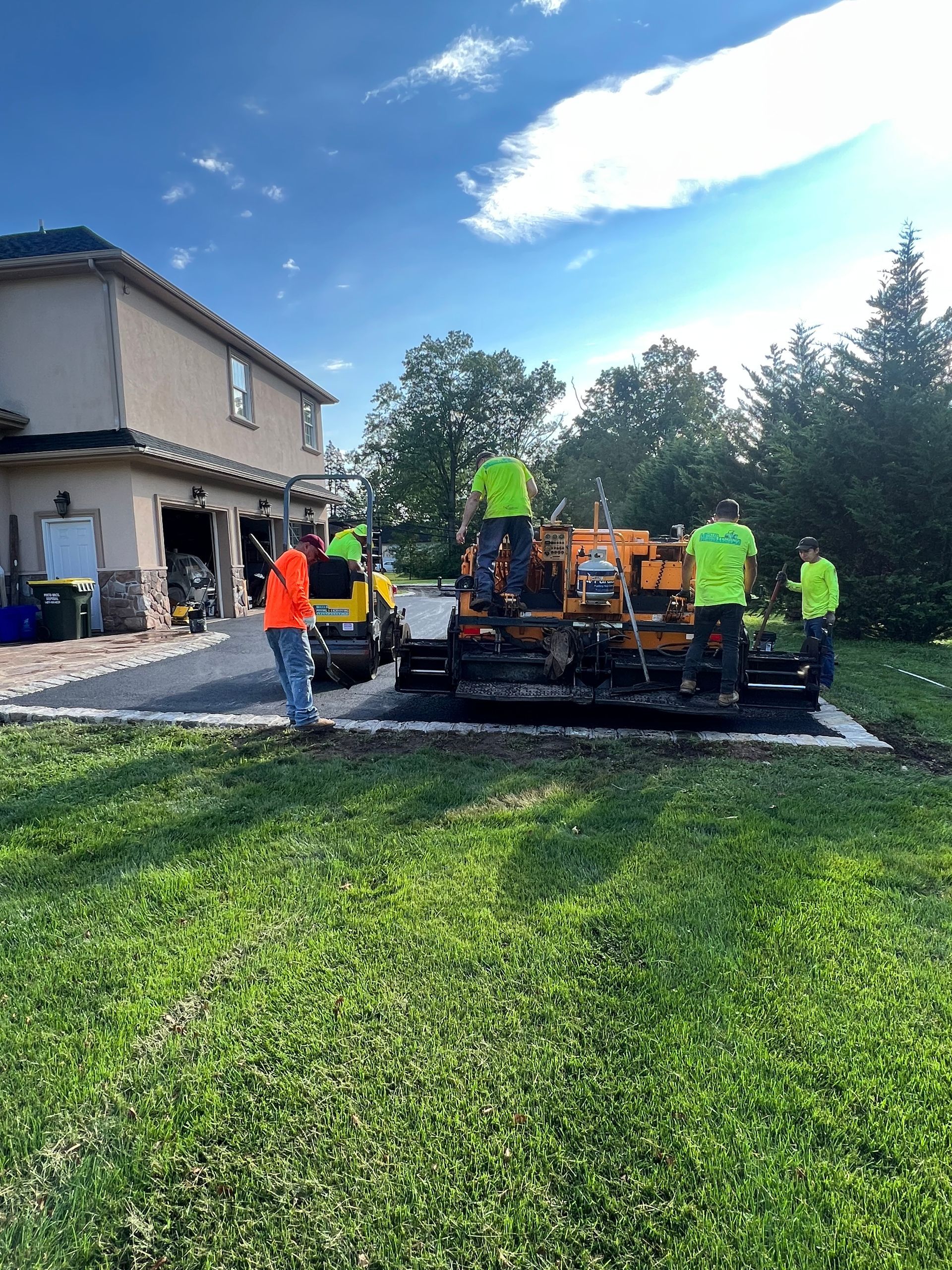 A group of people are working on a driveway in front of a house.