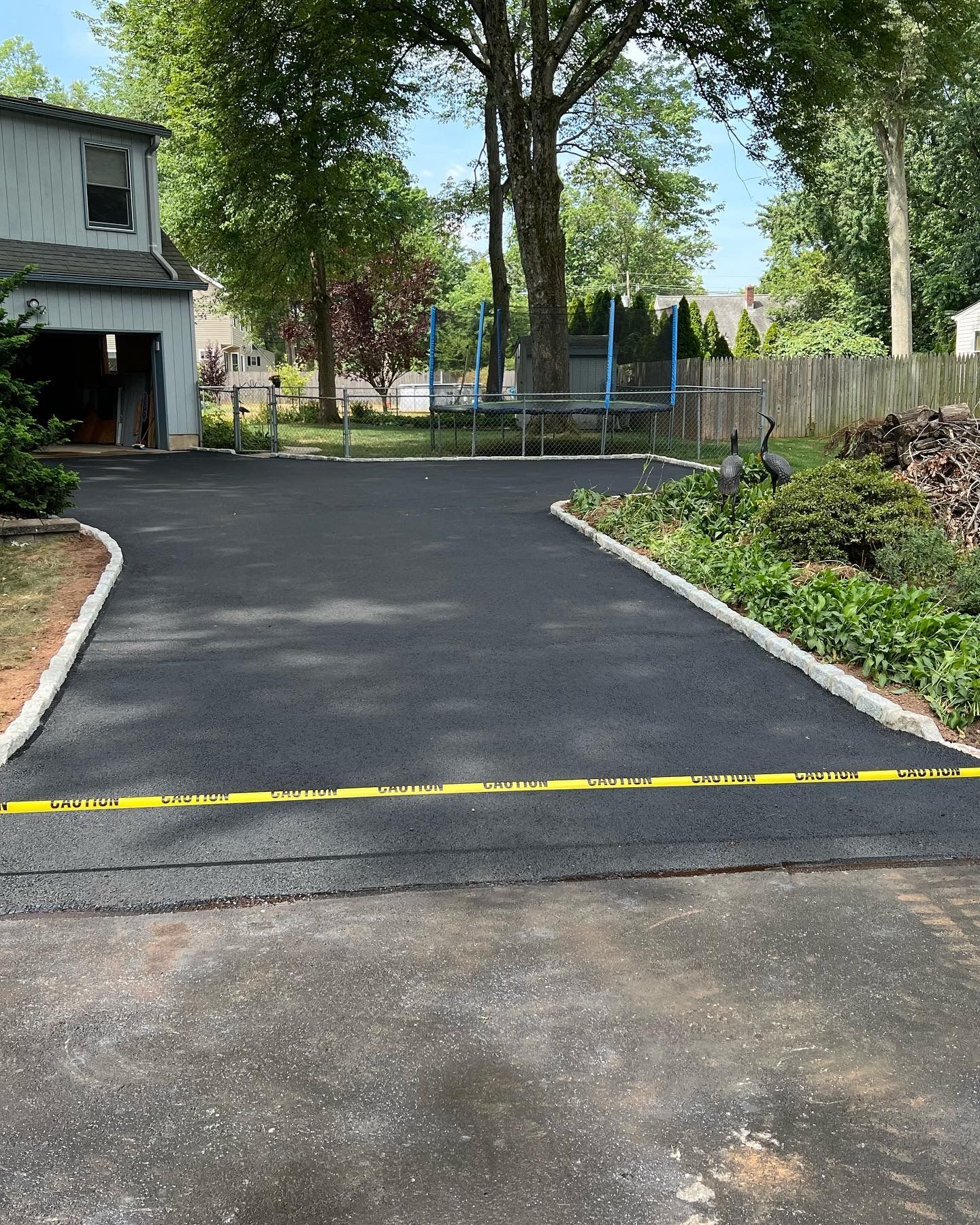 A driveway leading to a house with a trampoline in the backyard.