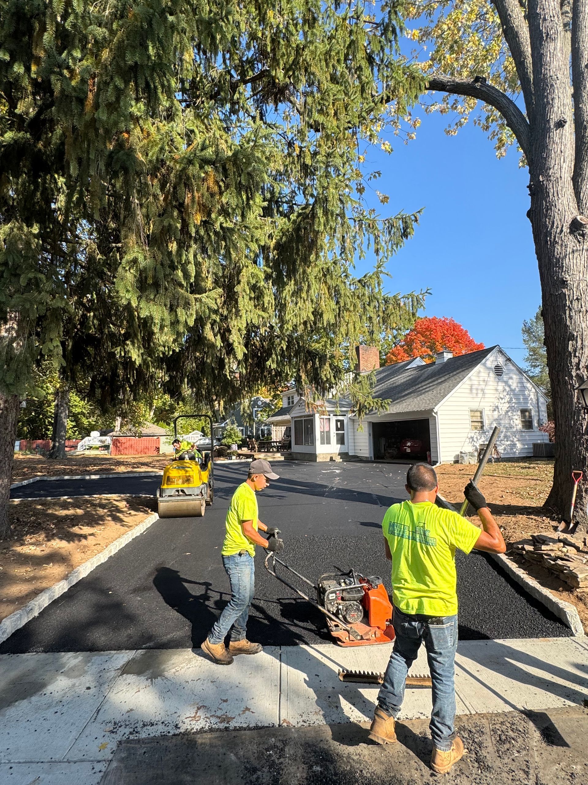 Two men are working on a driveway in front of a house.