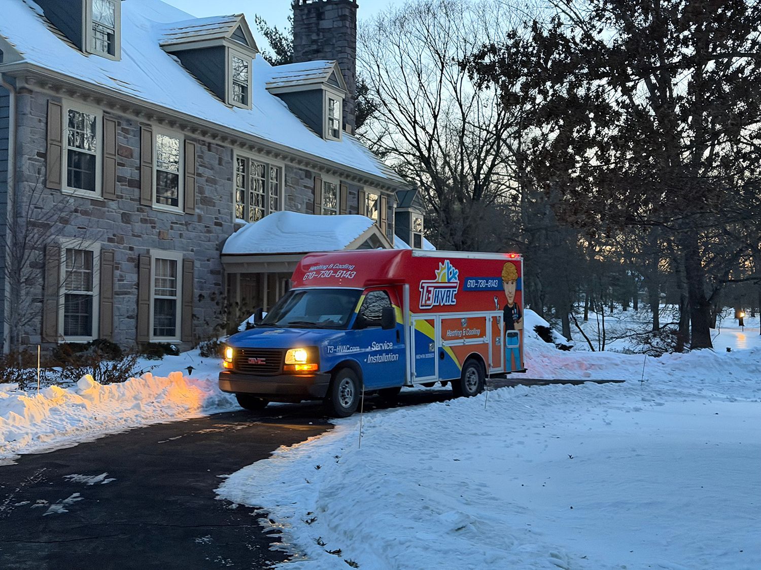 A colorful, branded truck is parked in a snow-covered driveway in front of a stone house on a winter day.