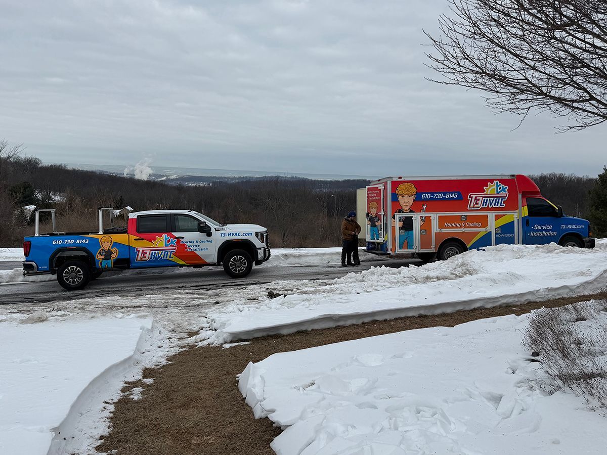 A brightly colored utility truck and a branded service trailer parked on a snowy, elevated roadside overlooking a valley.