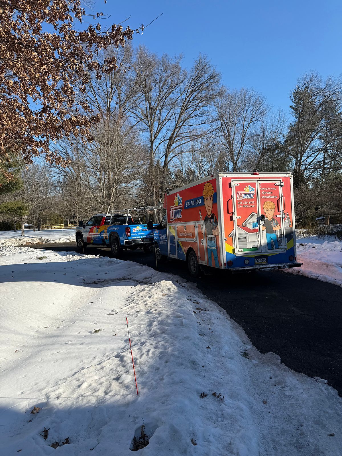 A blue pickup truck towing a brightly colored, branded television news van on a snow-covered residential road.