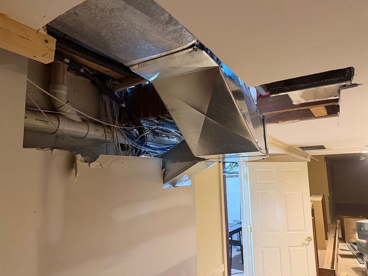 A view of a home ceiling opened up to reveal metallic HVAC ductwork and internal structural framing.