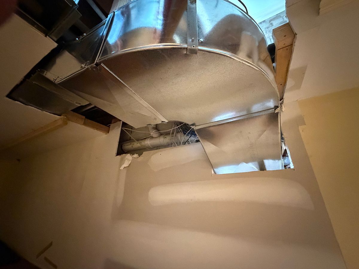 An unfinished ceiling showing silver metal HVAC ductwork exposed through a rectangular opening in white drywall.