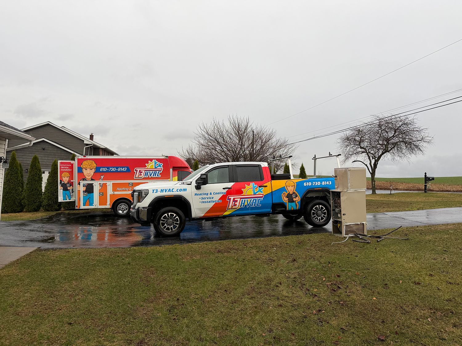 A brightly colored, branded work truck and trailer parked on a wet driveway in front of a residential home.