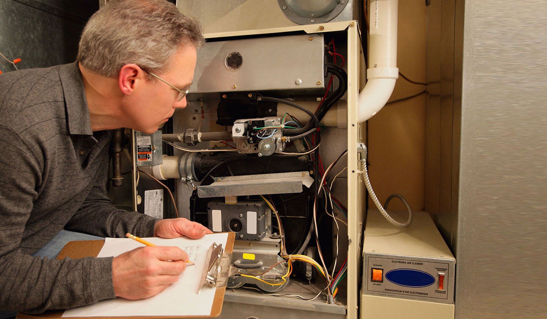 A person in a gray shirt inspecting an open furnace while writing on a clipboard.