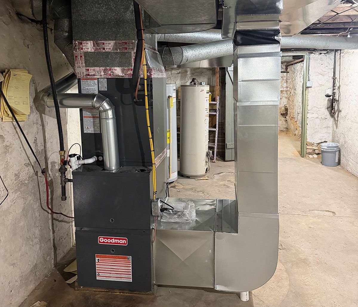 A charcoal furnace with ductwork and metal piping, installed in a residential basement with unfinished stone walls.