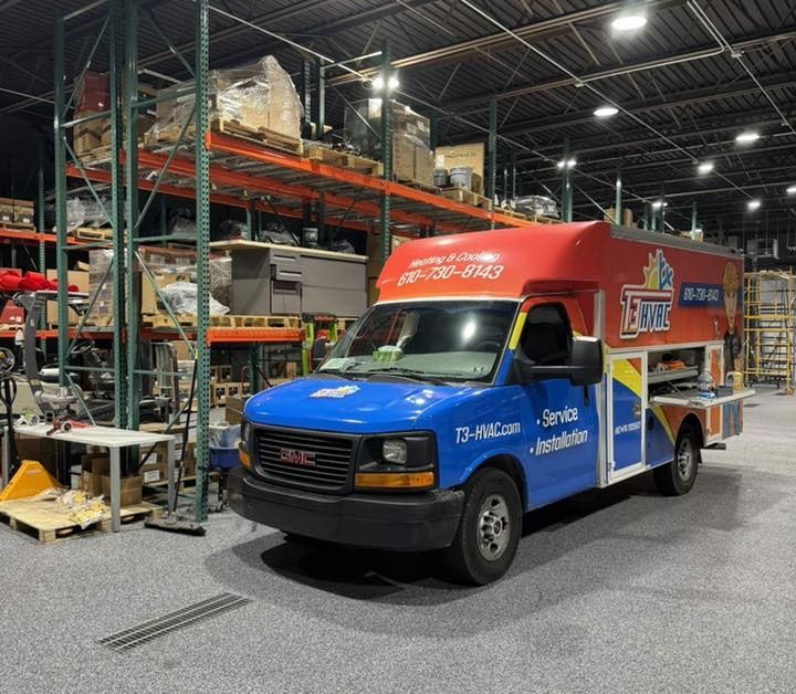 A bright blue, red, and white GMC service van parked inside a warehouse with tall storage shelving units in the background.