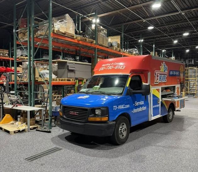 A bright blue, red, and white GMC service van parked inside a warehouse with tall storage shelving units in the background.