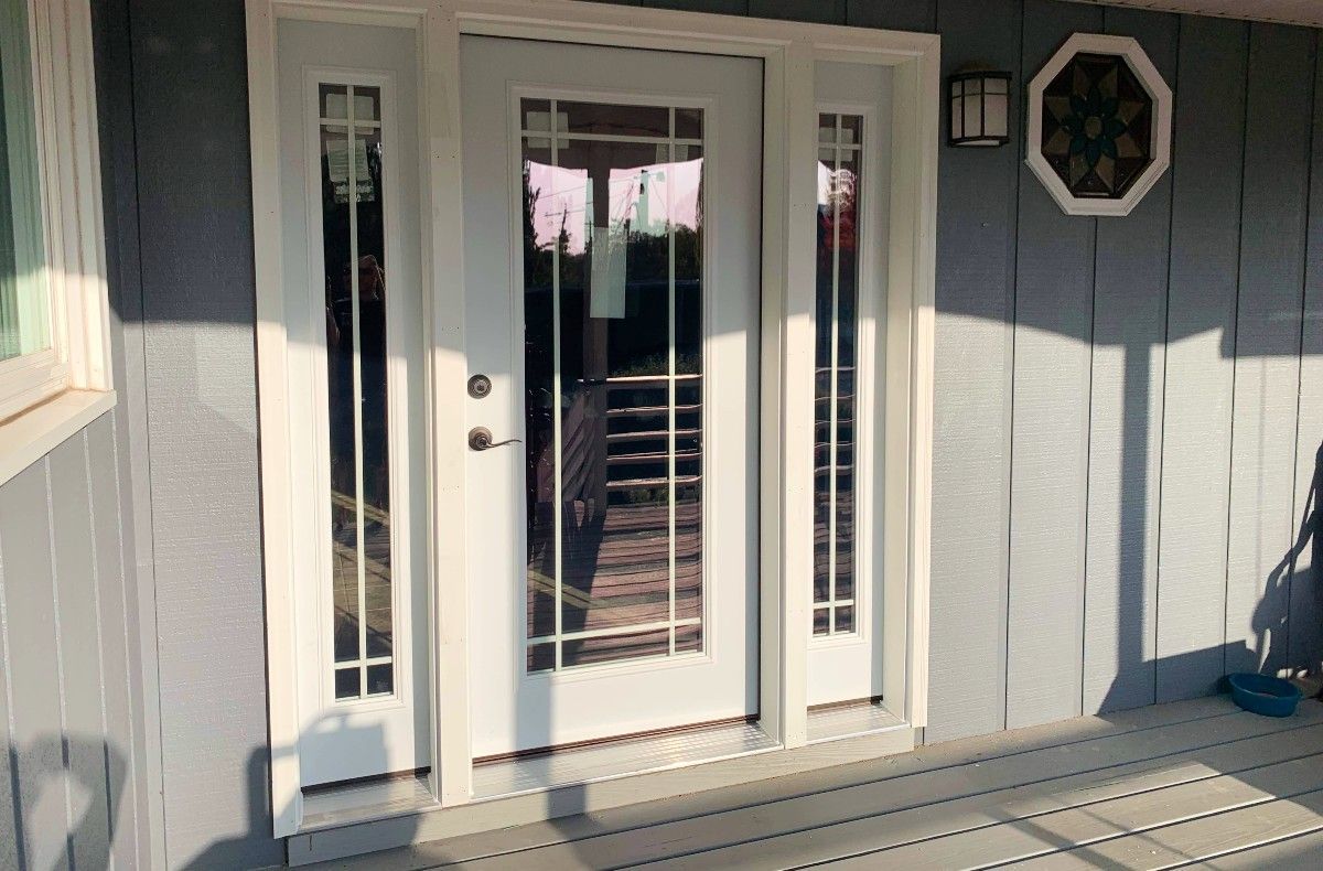 White front door with sidelights on a gray house porch in sunlight