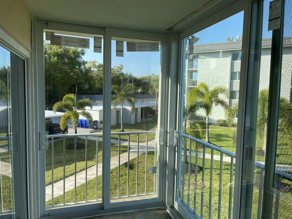 Sunroom with glass sliding doors overlooking a green lawn and palm trees on a sunny day.