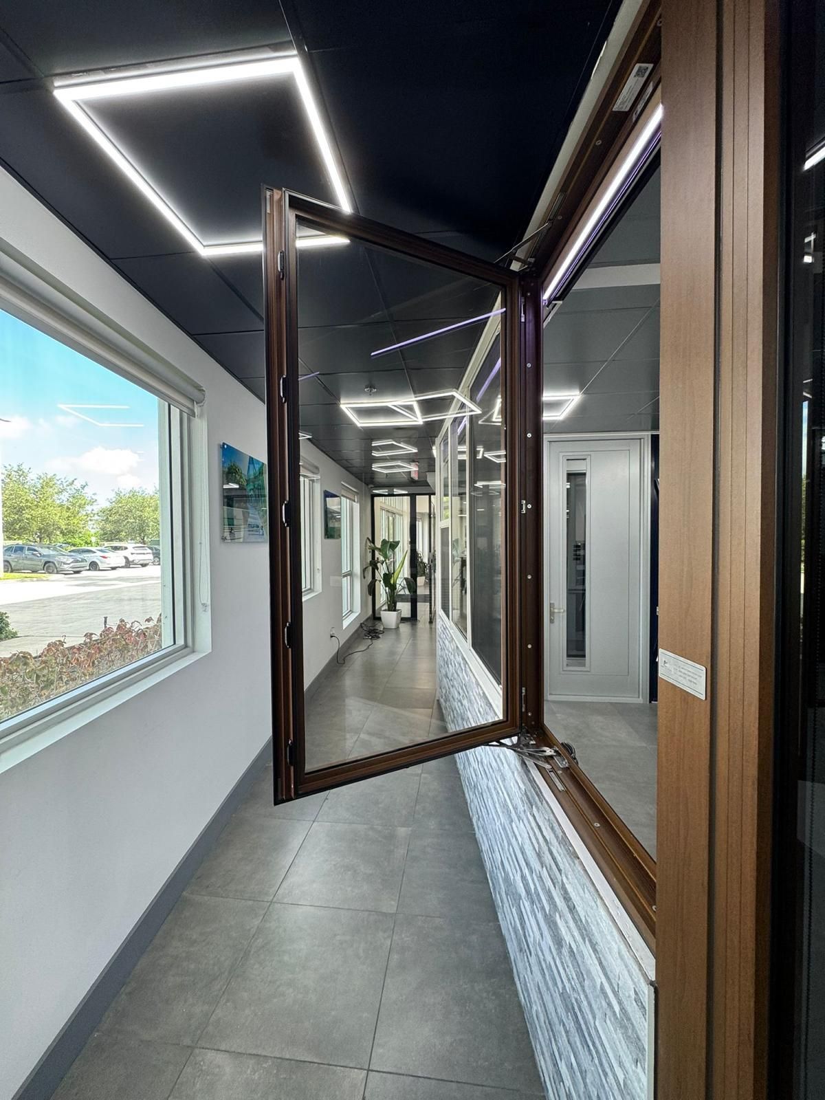 A brown-framed window is open in a showroom; the window is on a white brick wall, displaying the outside view.