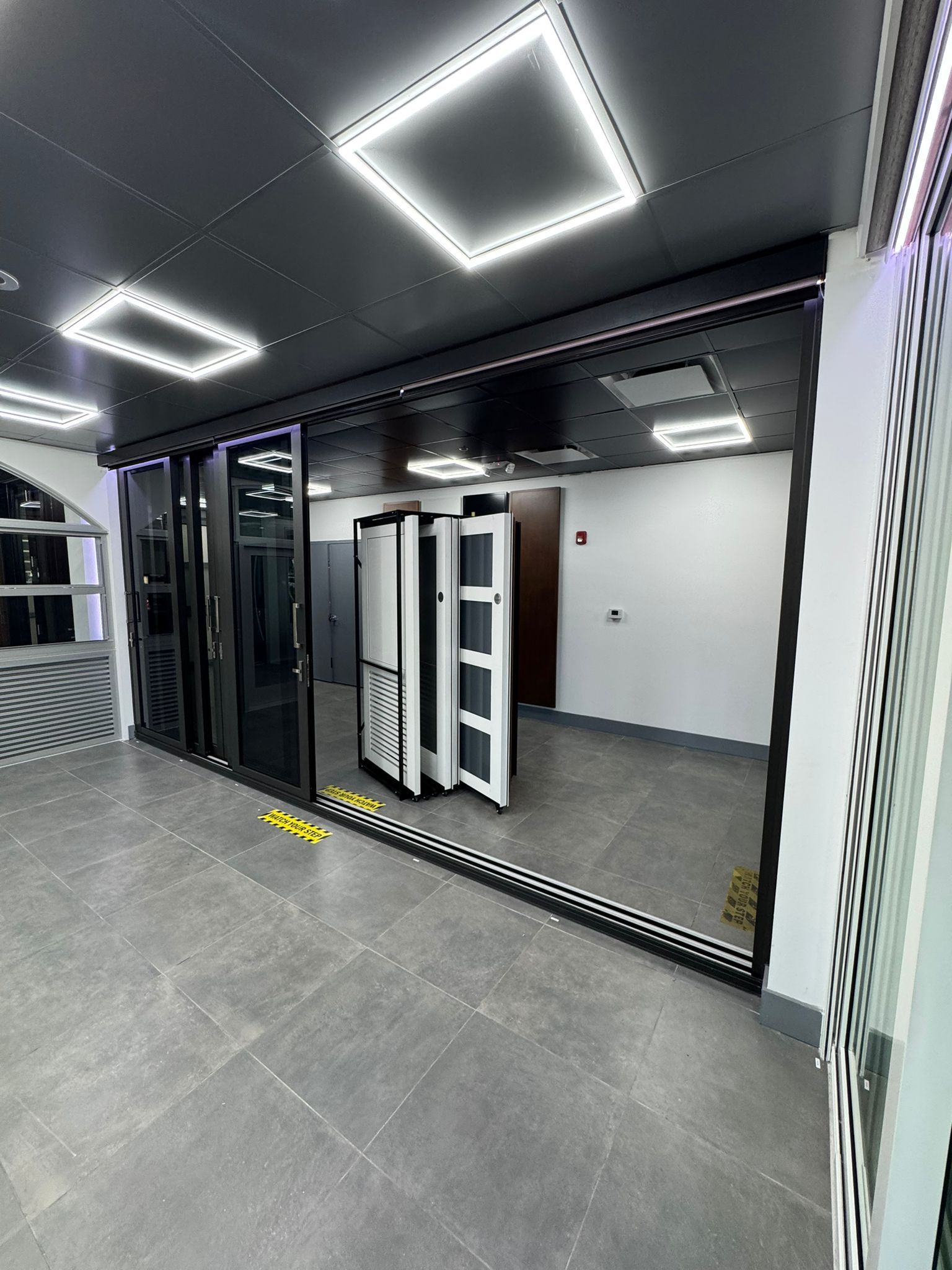 Room with folding black and white doors, gray floor, black ceiling with square lights.
