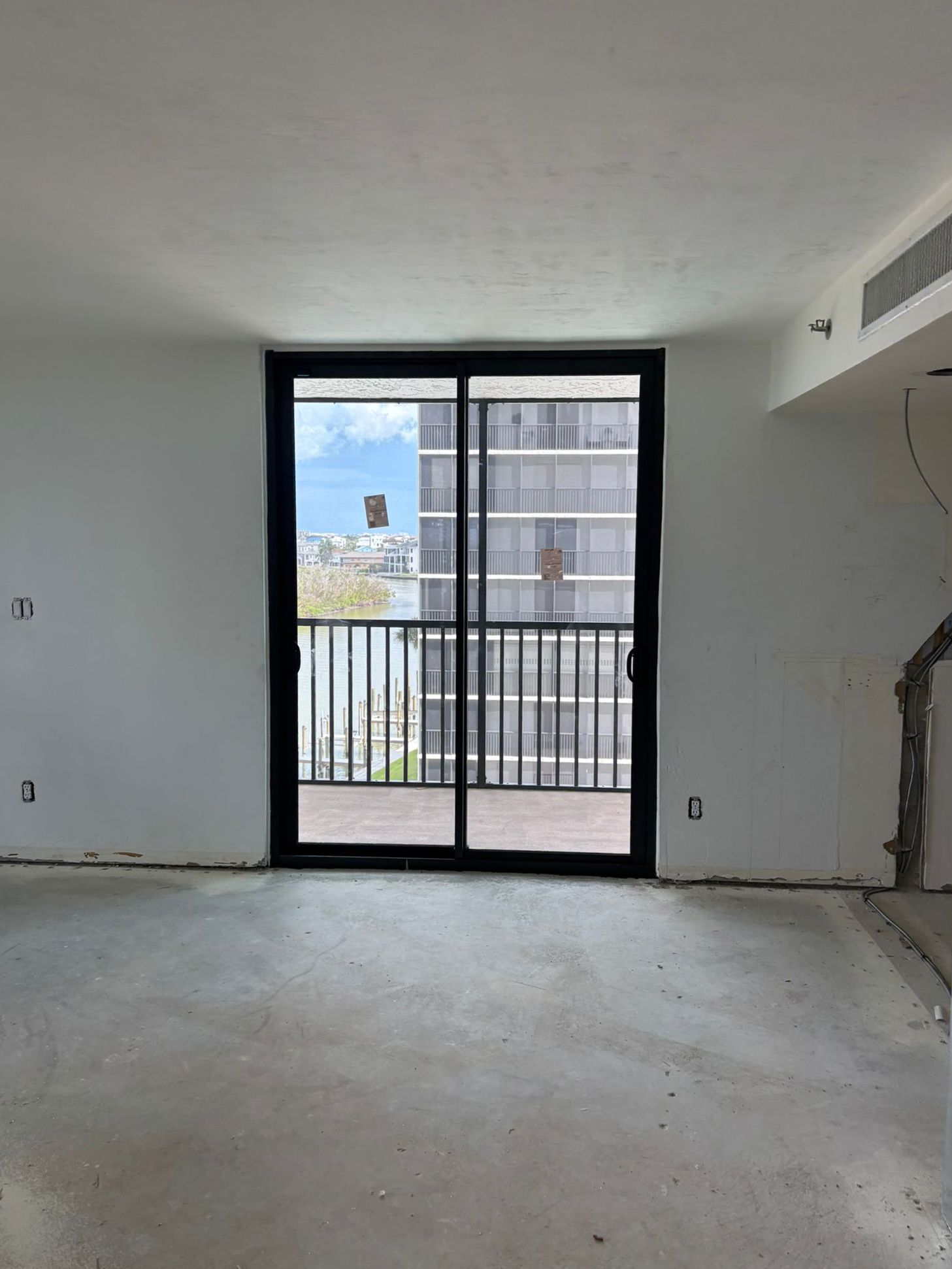 An empty room with a sliding glass door, offering a balcony view of buildings.