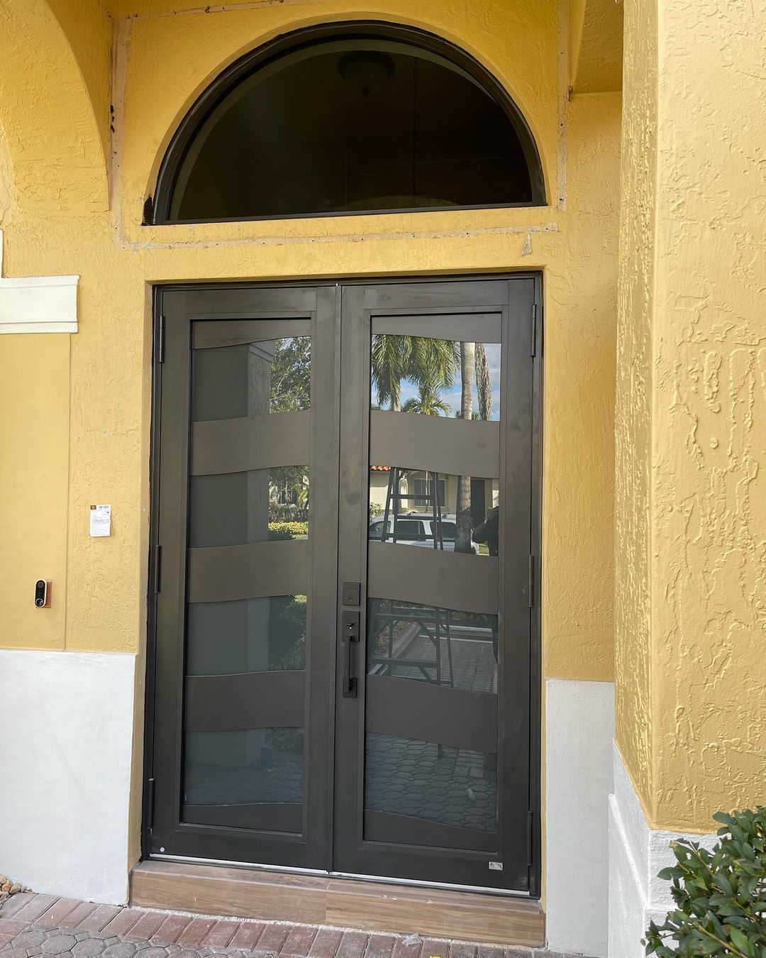 Double dark gray front doors with glass panels under a half-circle window, set in a tan stucco facade.