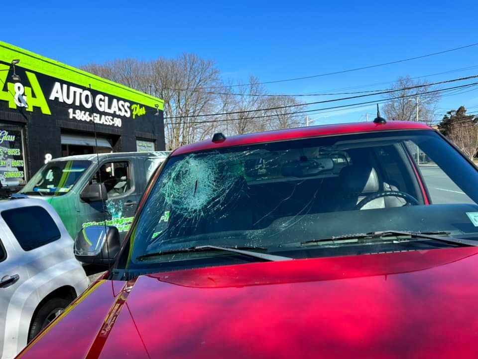 a red car with a broken windshield is parked in front of an auto glass shop