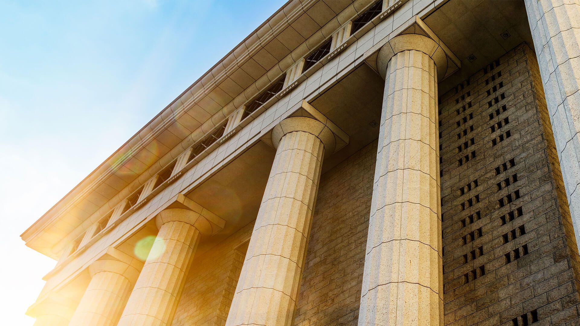 Low-angle view of a stone-columned classical building with sunlight and lens flare