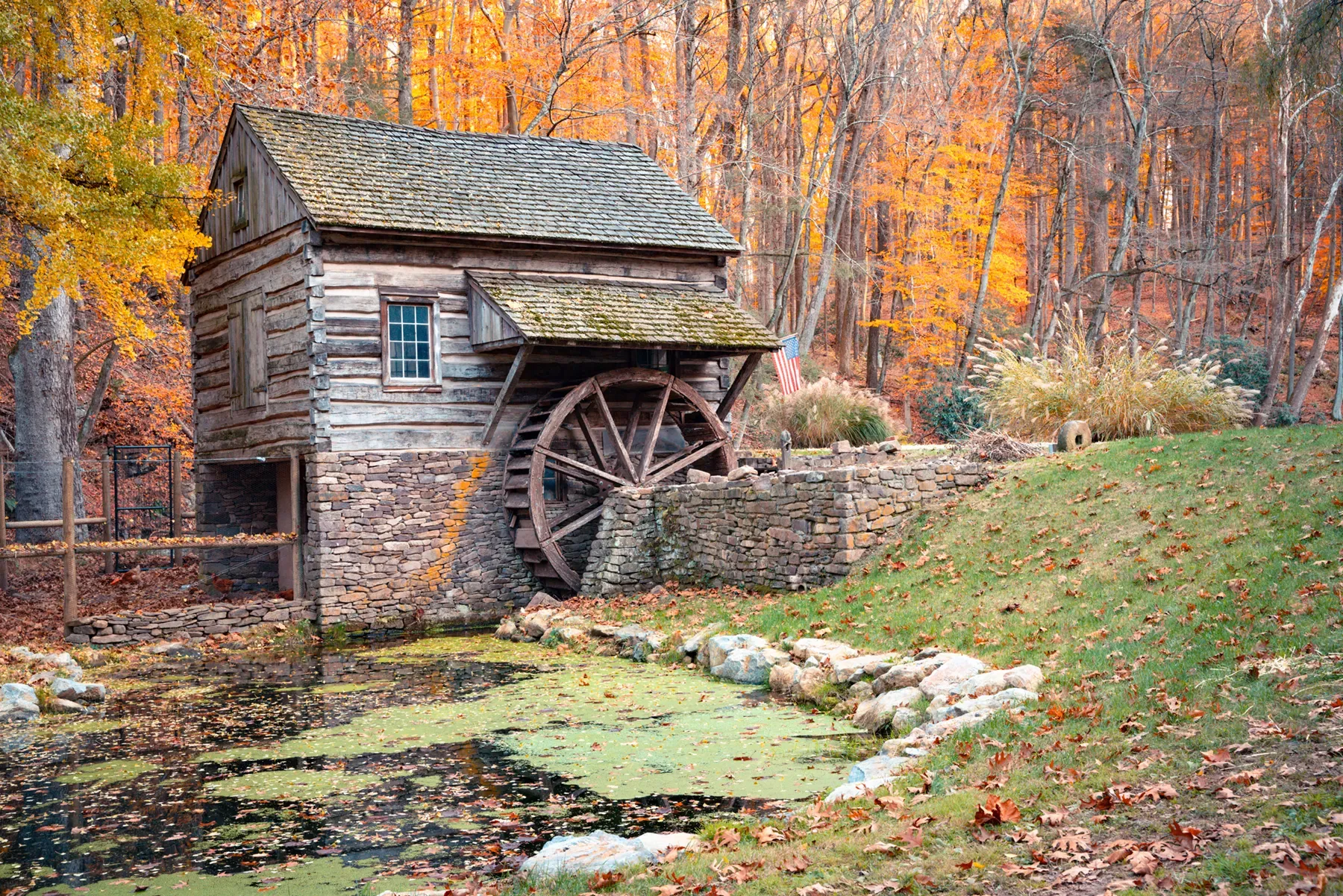 Old stone watermill with a large wheel beside a small stream in an autumn forest