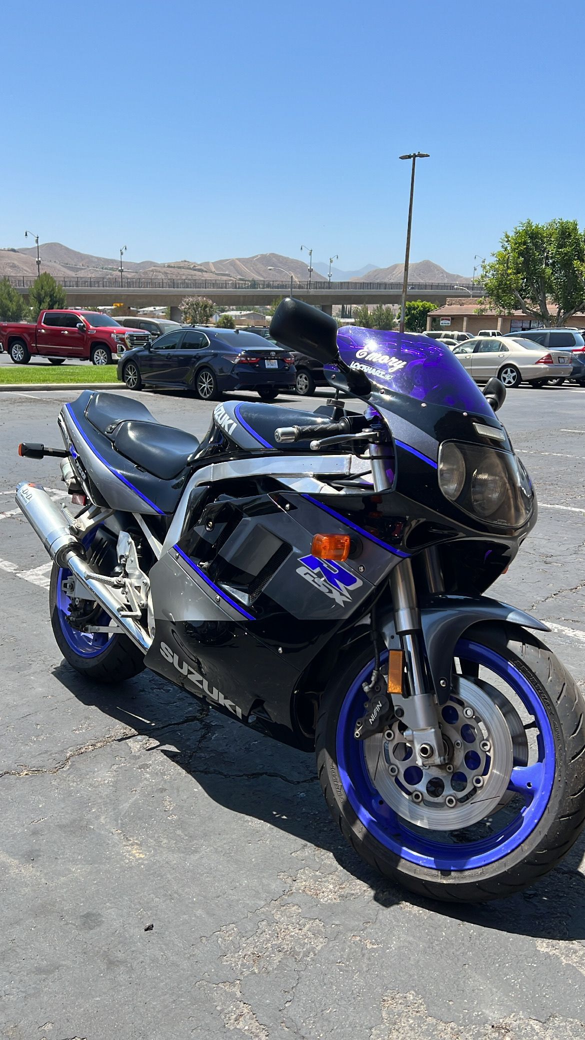 Suzuki motorcycle, blue and black fairing, parked in a sunny lot.