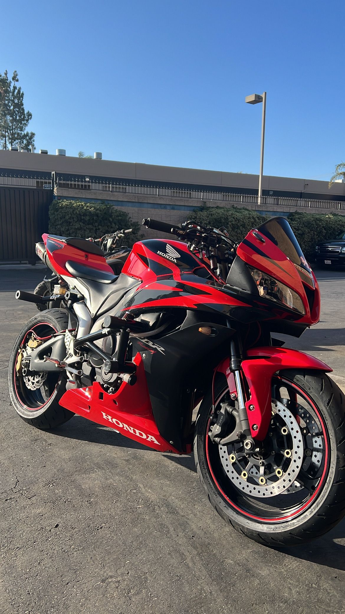 Red and black sport motorcycle parked on asphalt in front of buildings and a blue sky.
