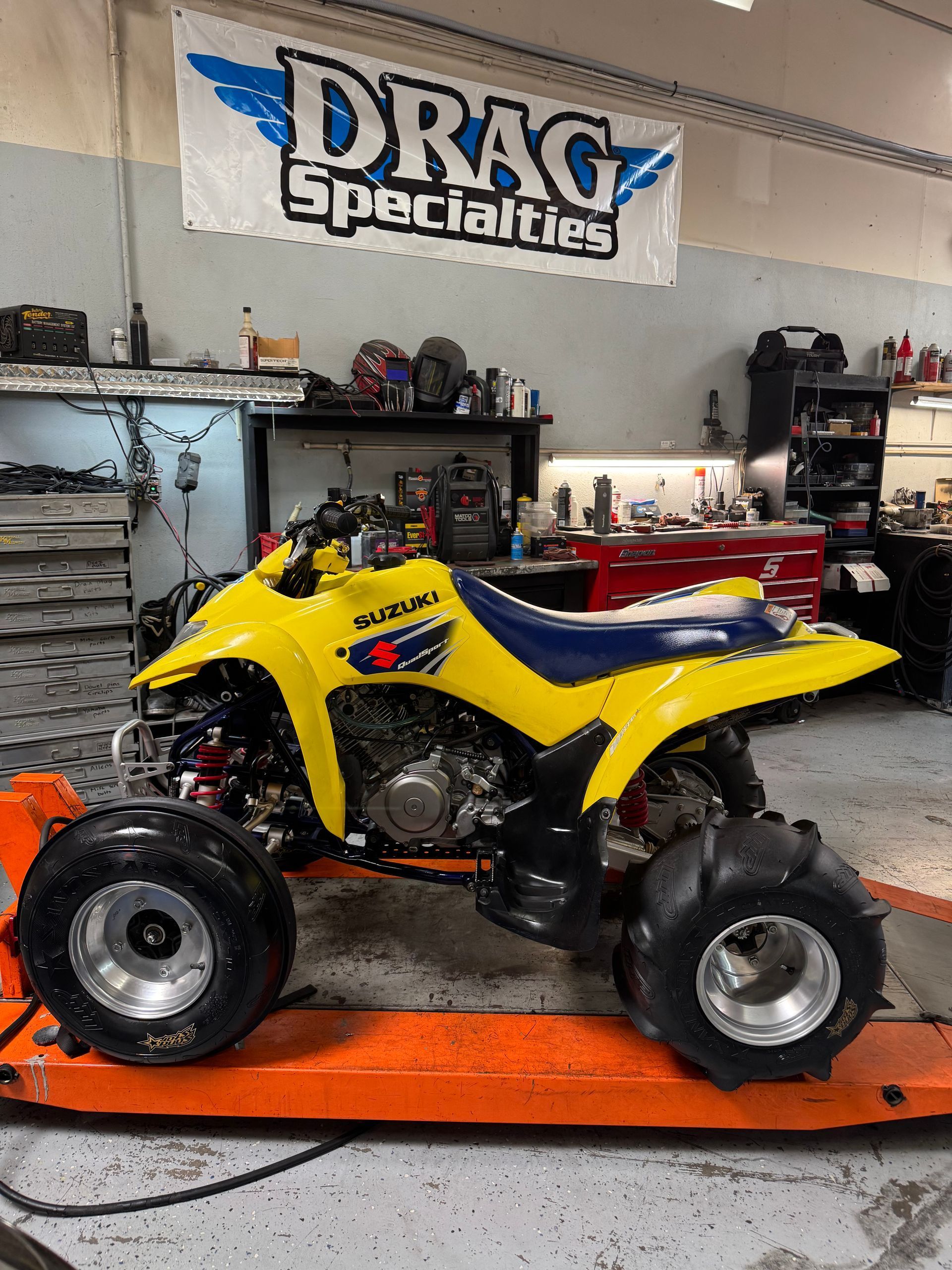 Yellow Suzuki ATV with sand tires on a lift in a garage with a 