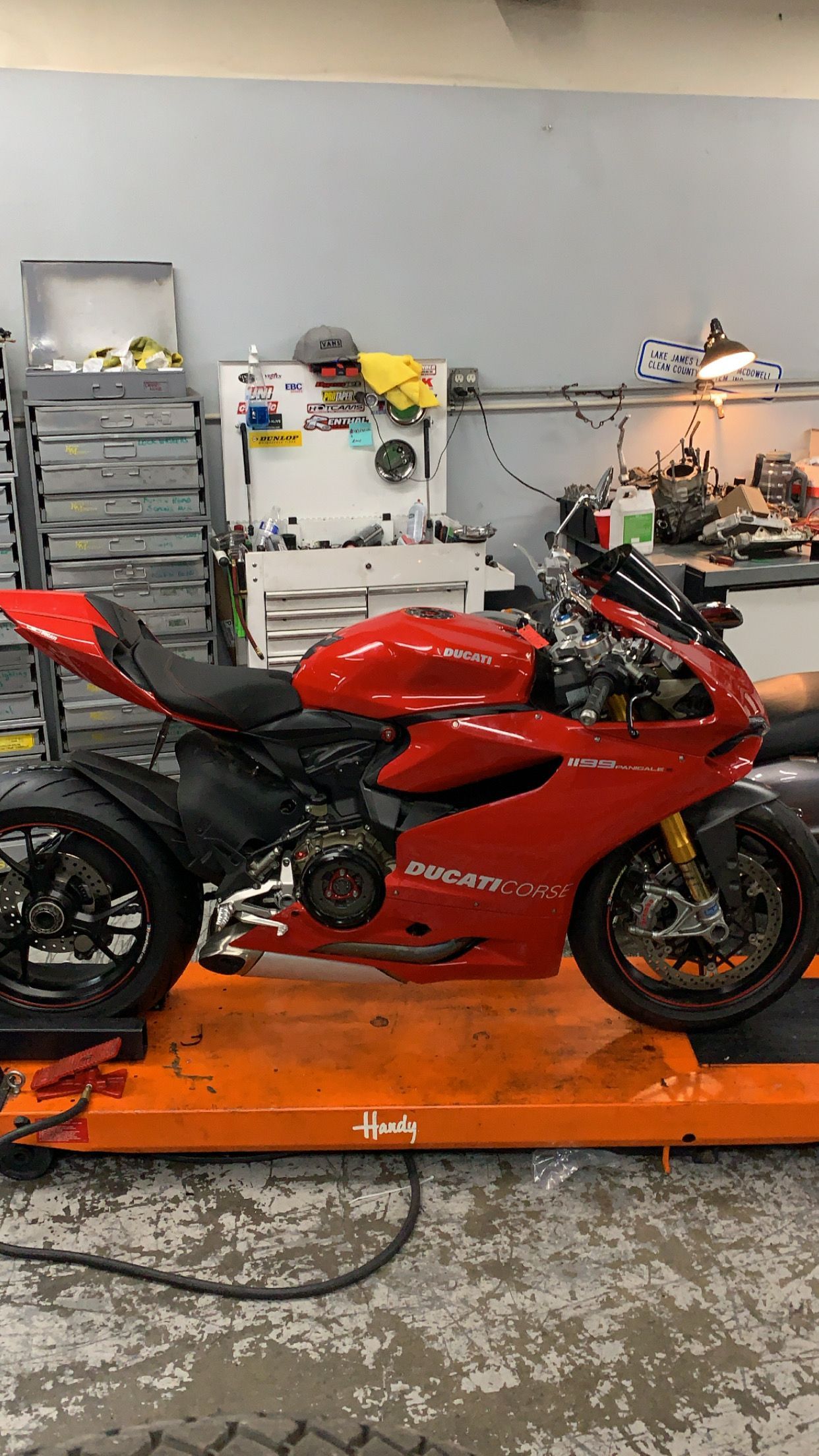 Red Ducati motorcycle on an orange lift inside a shop; tools and equipment are in the background.