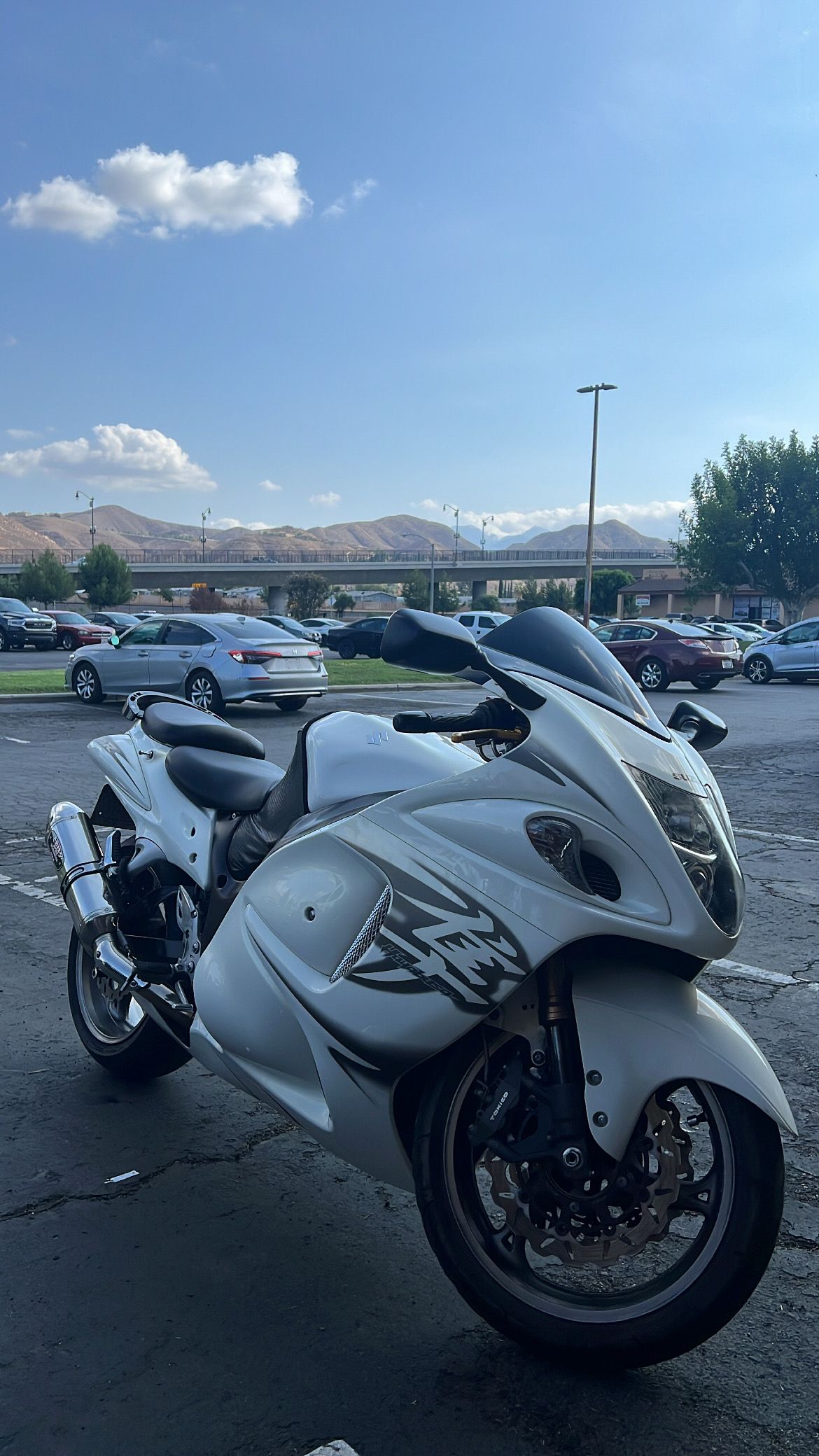 White Suzuki Hayabusa motorcycle parked in a parking lot with blue sky and mountains in background.
