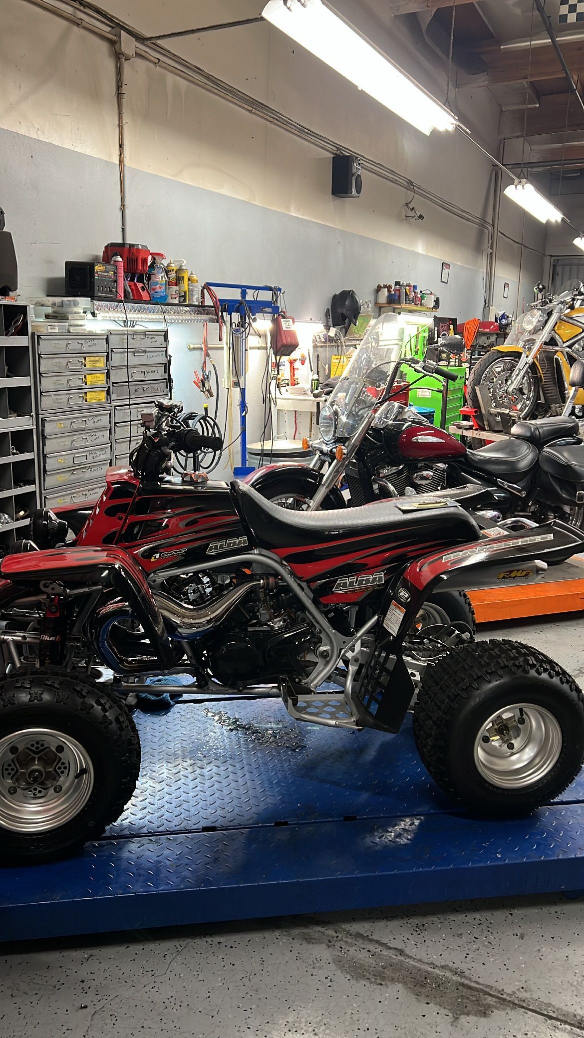Red and black ATV with chrome wheels inside a workshop.