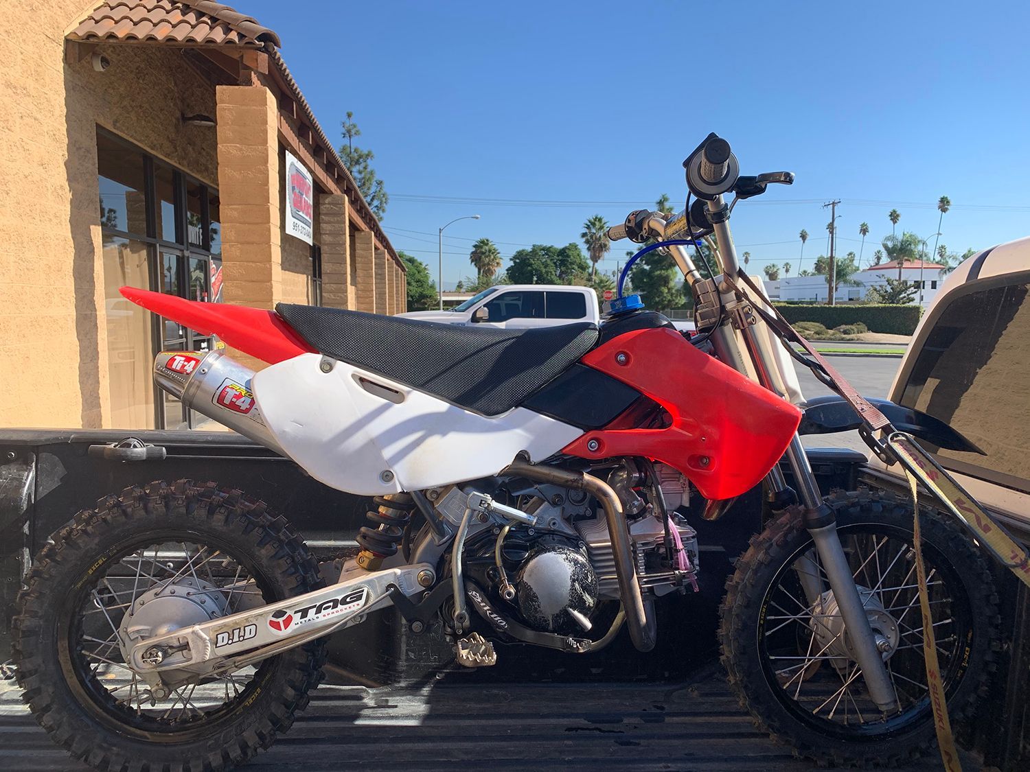 Dirt bike with red and white bodywork, loaded in a truck bed under a clear sky.