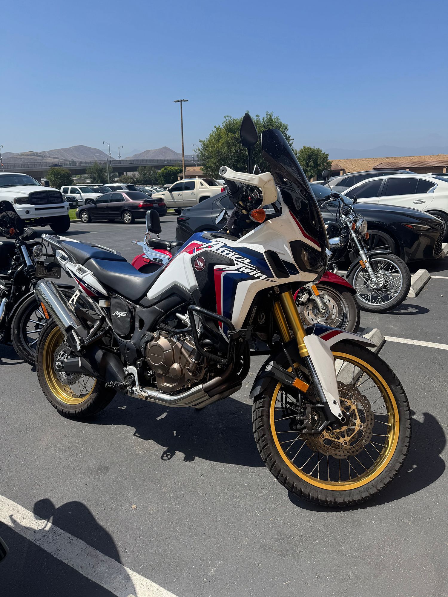 White, red, and blue Honda Africa Twin motorcycle parked in a lot on a sunny day.