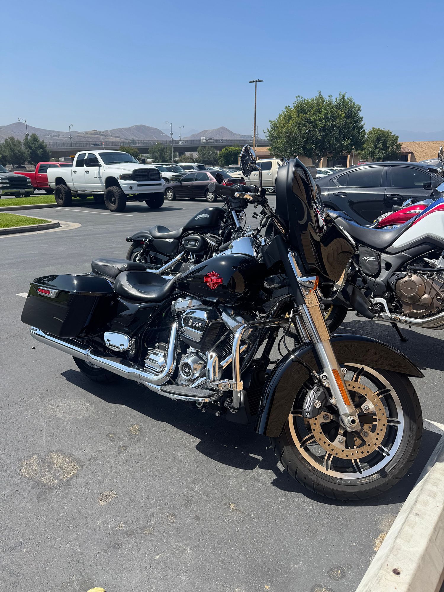 Black Harley-Davidson motorcycle parked in a parking lot on a sunny day, with other vehicles in the background.