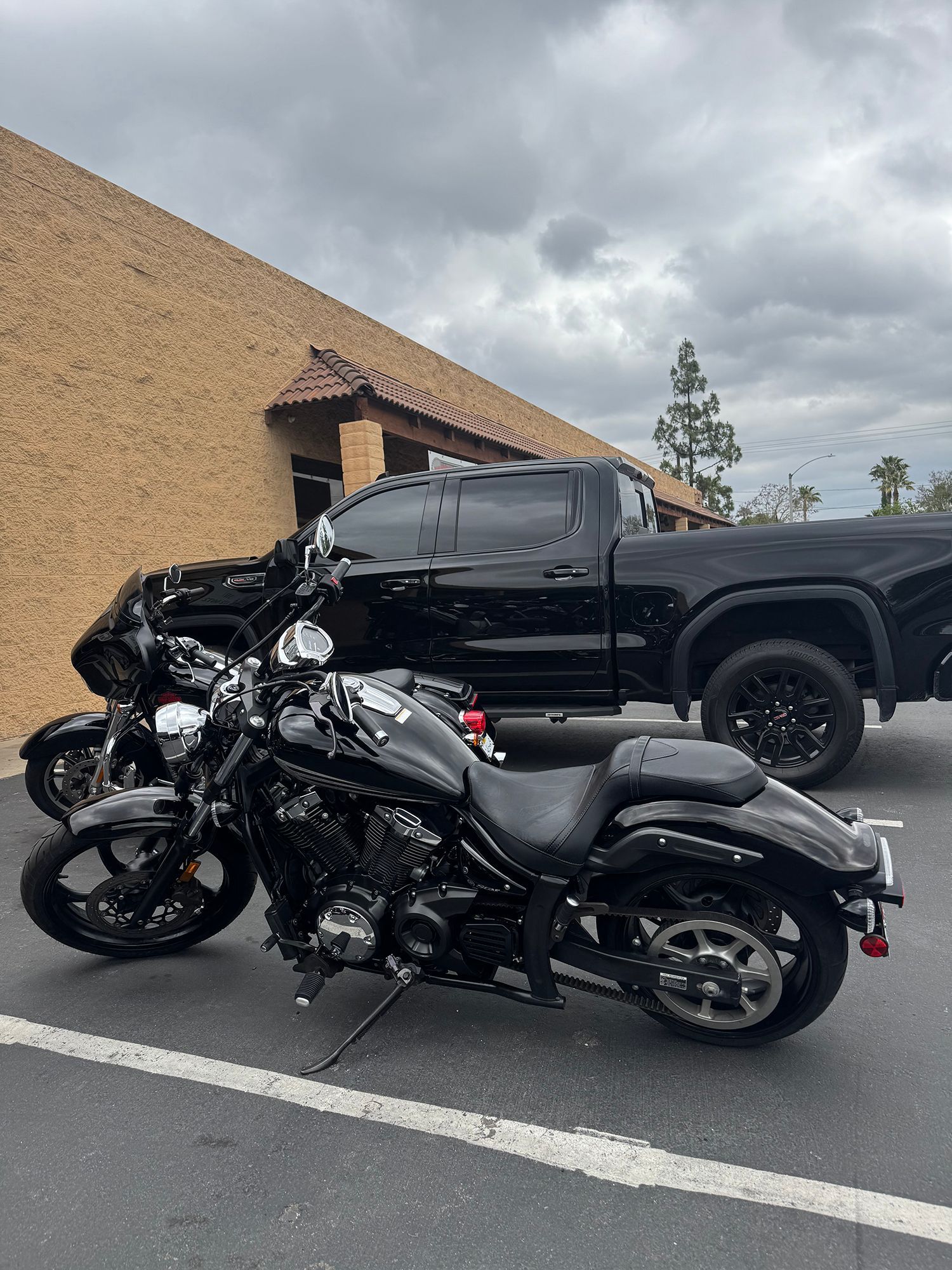 Black motorcycle parked in front of a black pickup truck next to a brick building on a cloudy day.
