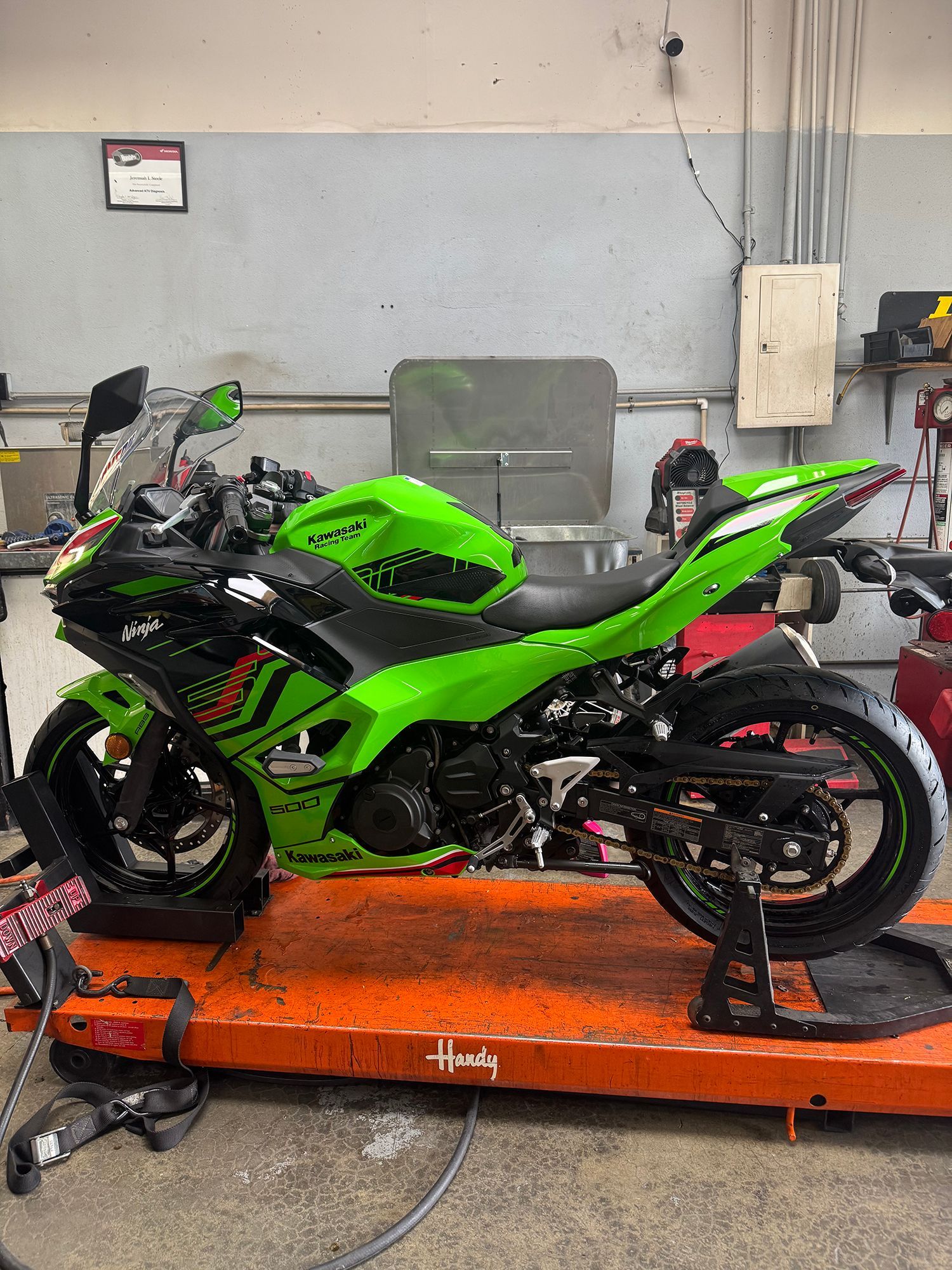Green Kawasaki Ninja motorcycle on an orange lift in a garage.